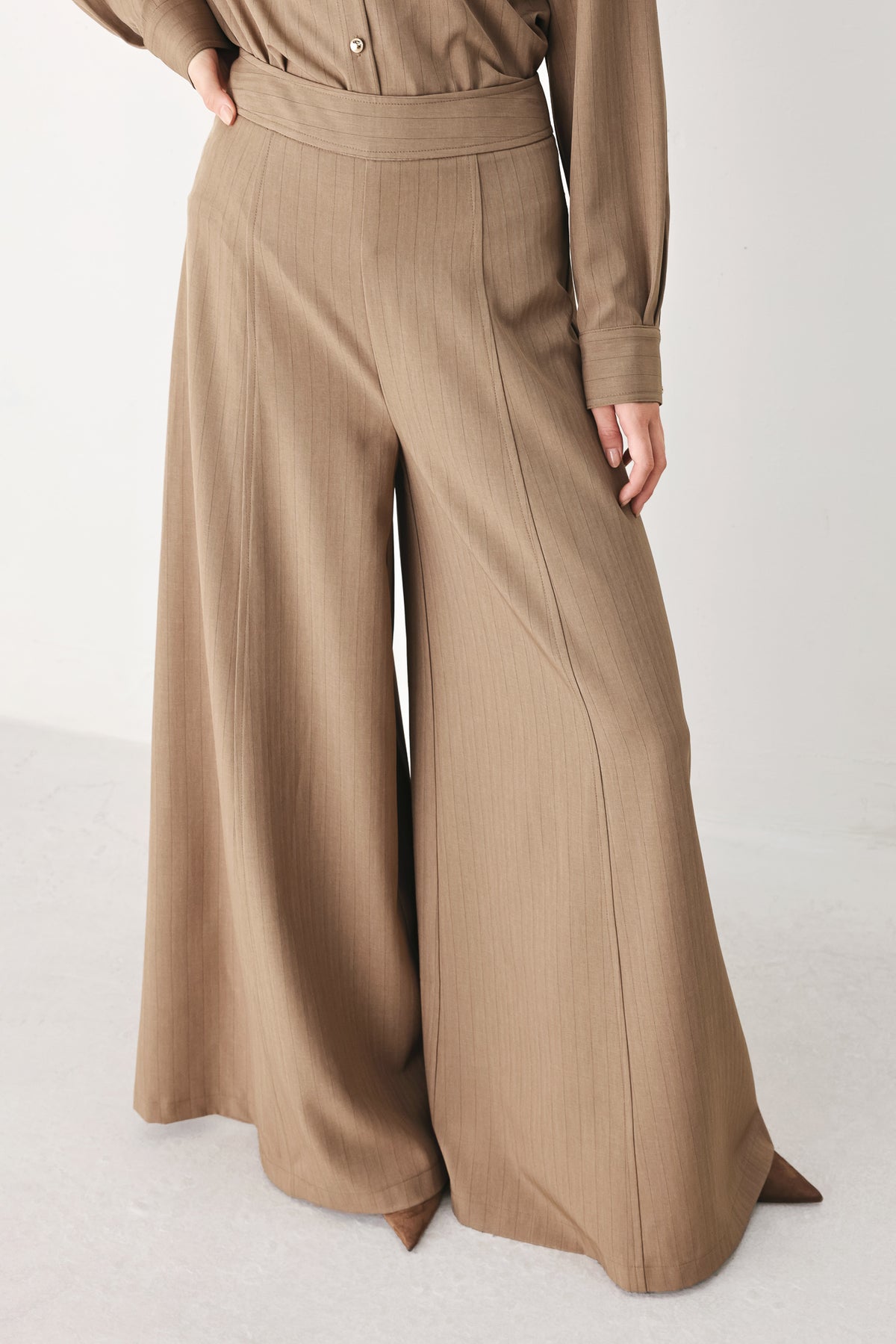 A person wearing high-waisted, wide-leg trousers in a warm taupe-brown color | FREEMARKET