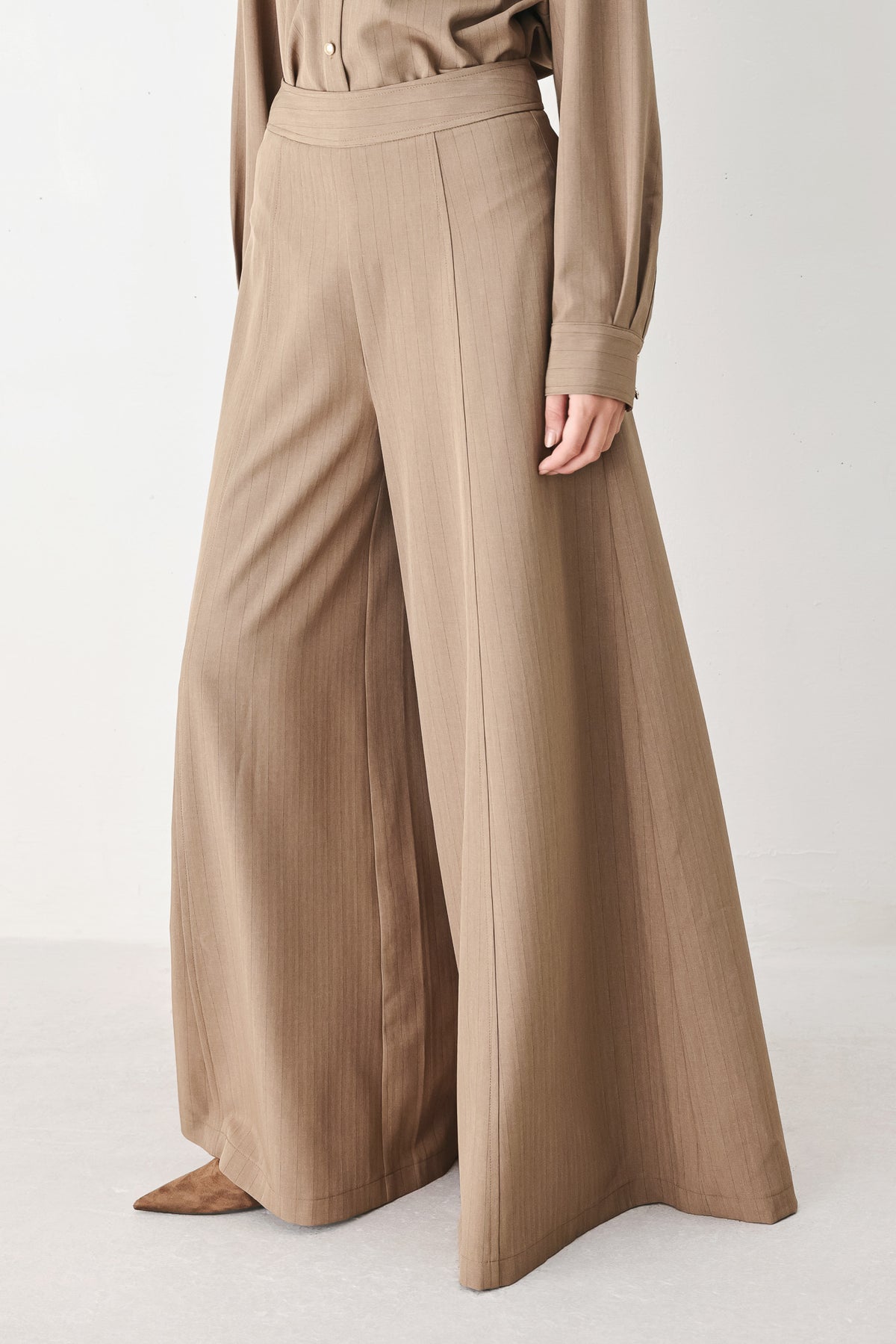 A person wearing high-waisted, wide-leg trousers in a warm taupe-brown color | FREEMARKET