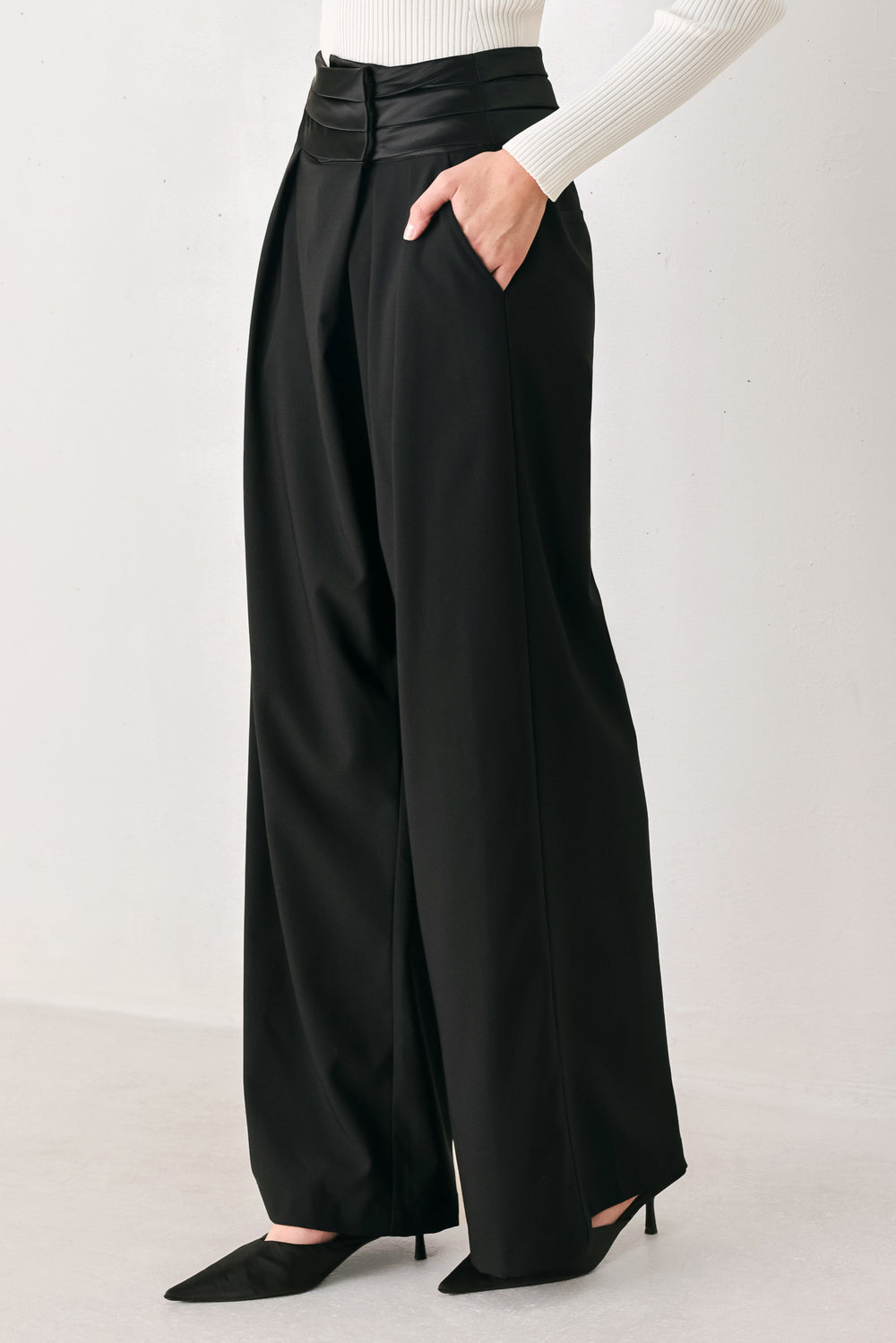 A model wearing high-waisted, wide-leg black trousers with a satin-like waistband | FREEMARKET