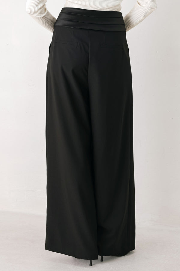 A model wearing high-waisted, wide-leg black trousers with a satin-like waistband | FREEMARKET