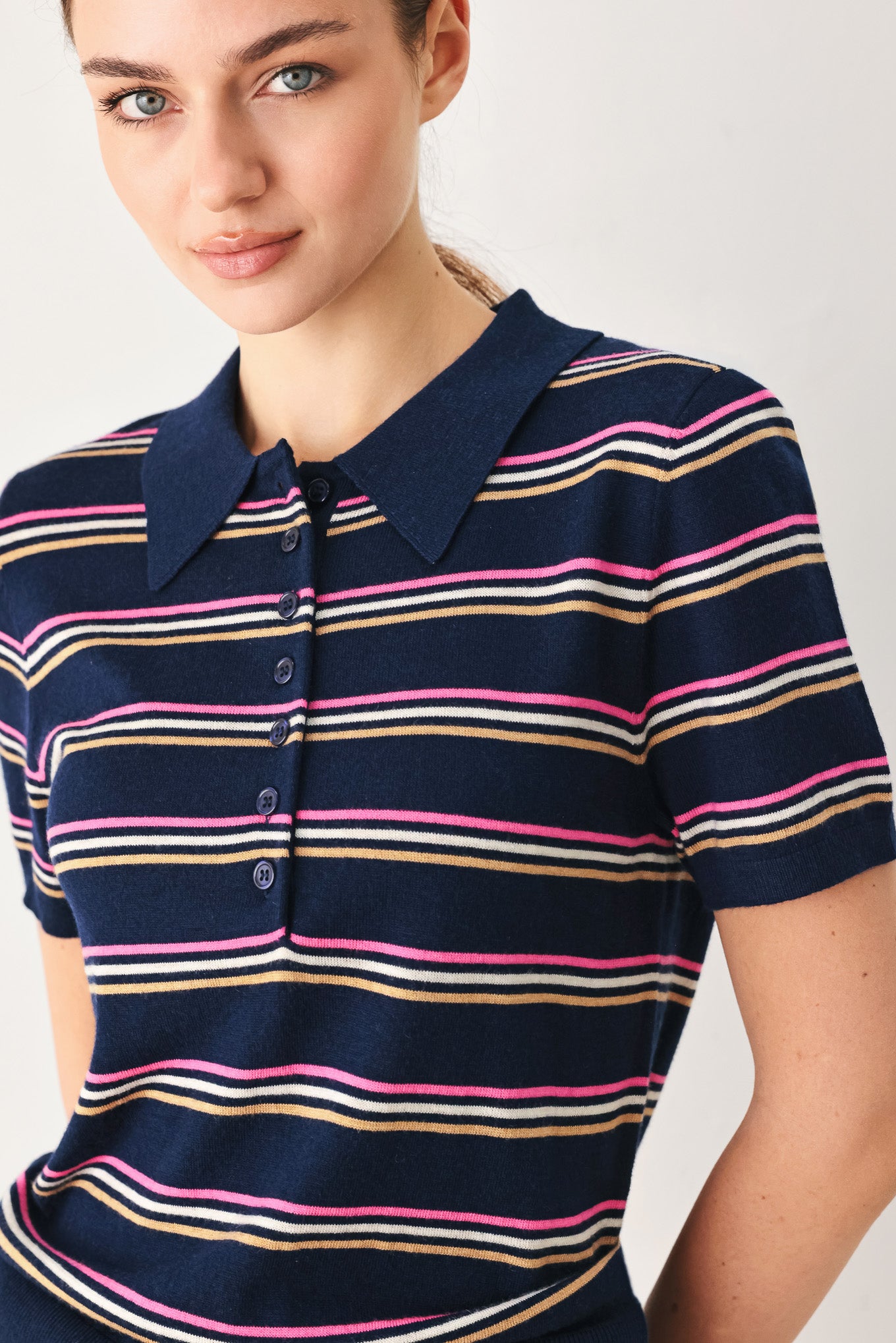 A woman wearing a navy blue short-sleeve polo shirt with thin horizontal stripes in pink, yellow, and white | FREEMARKET