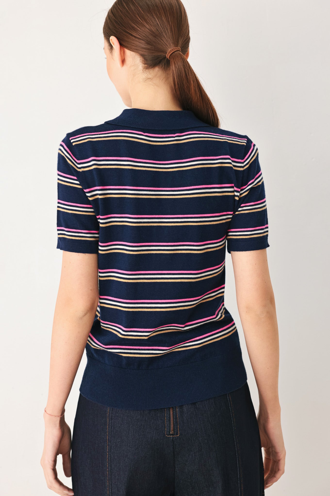 A woman wearing a navy blue short-sleeve polo shirt with thin horizontal stripes in pink, yellow, and white | FREEMARKET