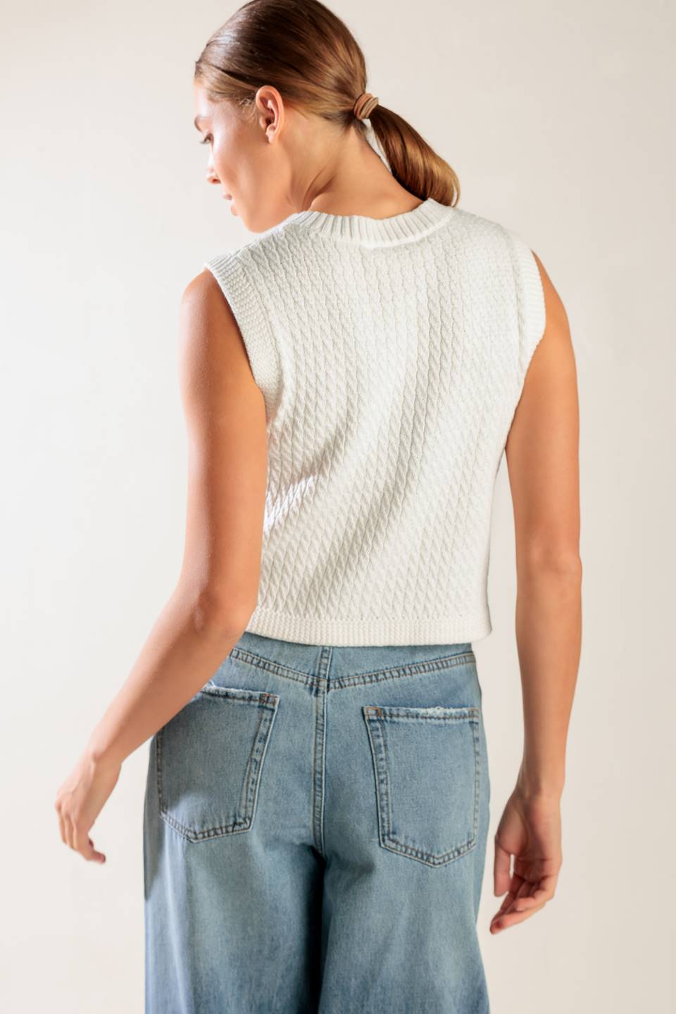 A white, sleeveless, sweater knit vest featuring round neckline and button down closure.