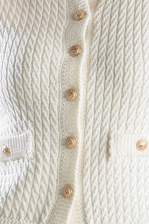 A white, sleeveless, sweater knit vest featuring round neckline and button down closure.