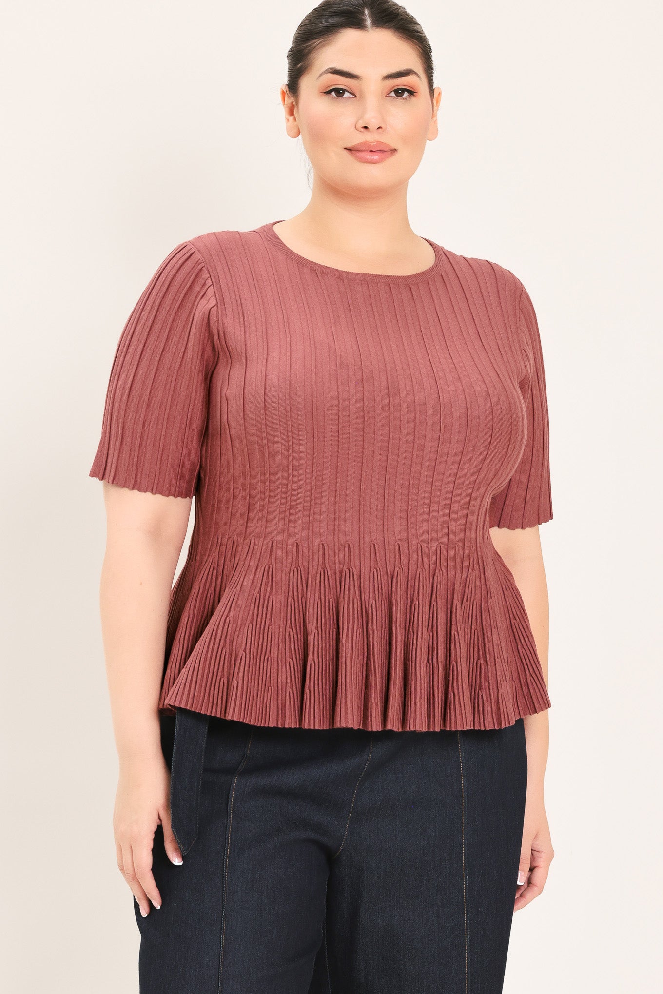 A woman modeling a short-sleeve, crew-neck top with a pleated texture and peplum hem in a dusty rose color | Plus Curve Flying Tomato