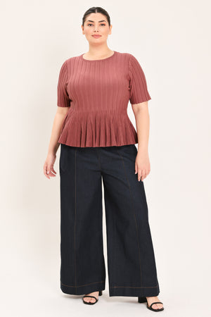 A woman modeling a short-sleeve, crew-neck top with a pleated texture and peplum hem in a dusty rose color | Plus Curve Flying Tomato