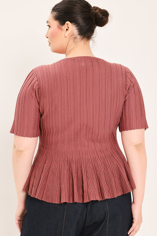 A woman modeling a short-sleeve, crew-neck top with a pleated texture and peplum hem in a dusty rose color | Plus Curve Flying Tomato
