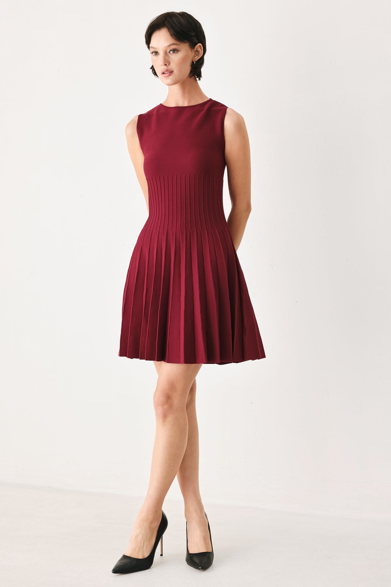 Woman wearing a burgundy sleeveless sweater knit mini dress with wide neckline, and pleated skirt | FREEMARKET