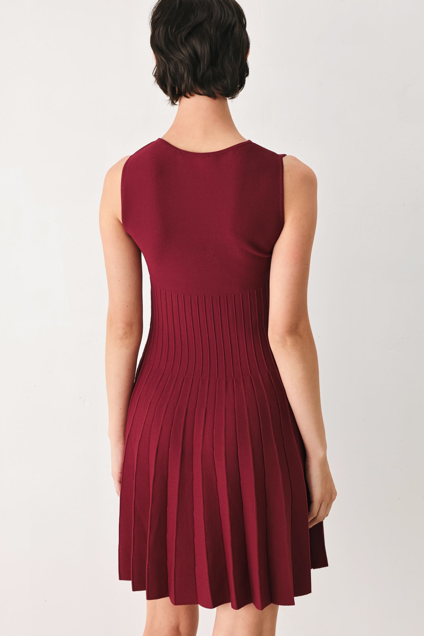 Woman wearing a burgundy sleeveless sweater knit mini dress with wide neckline, and pleated skirt | FREEMARKET