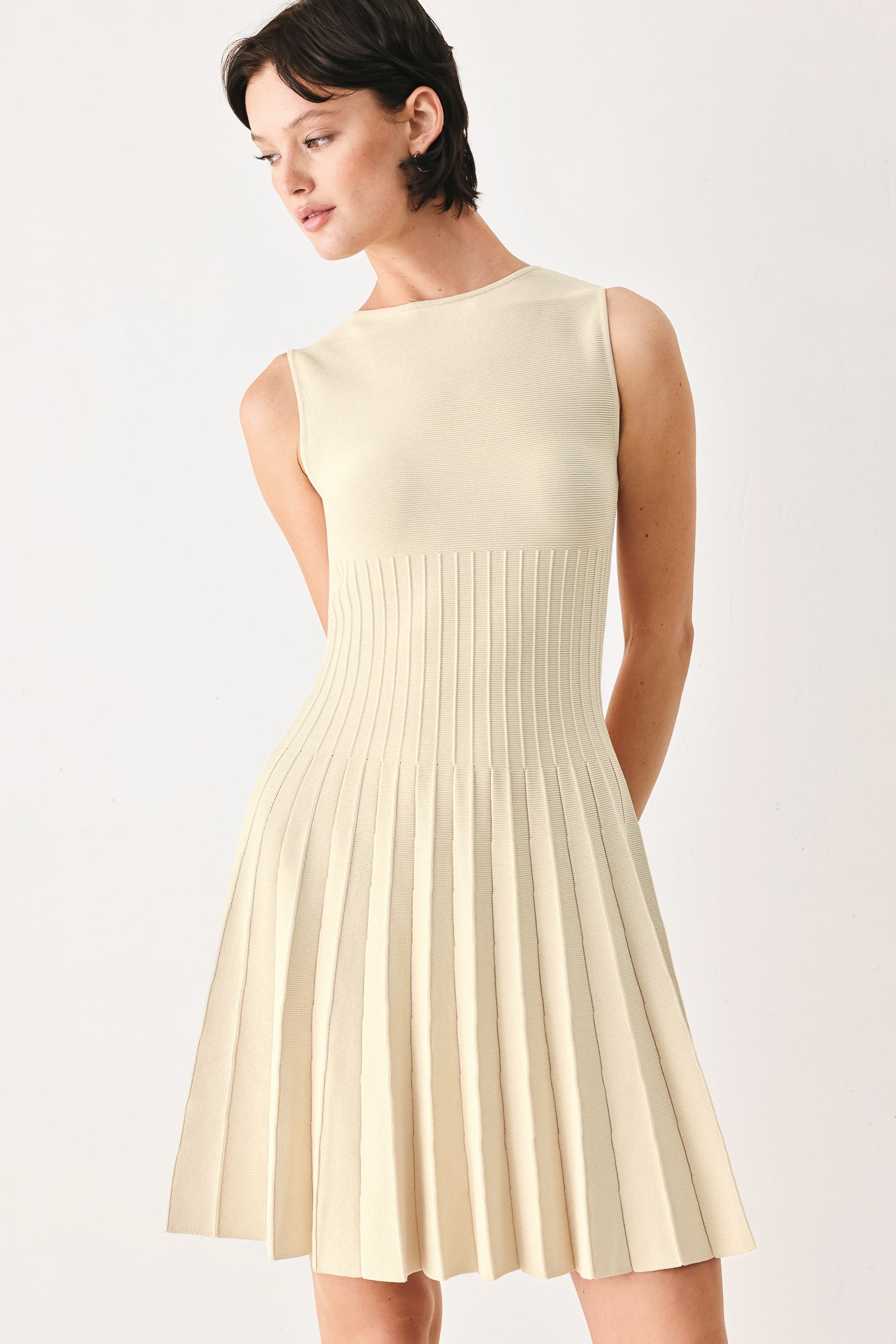 Woman wearing a ivory cream sleeveless sweater knit mini dress with wide neckline, and pleated skirt | FREEMARKET