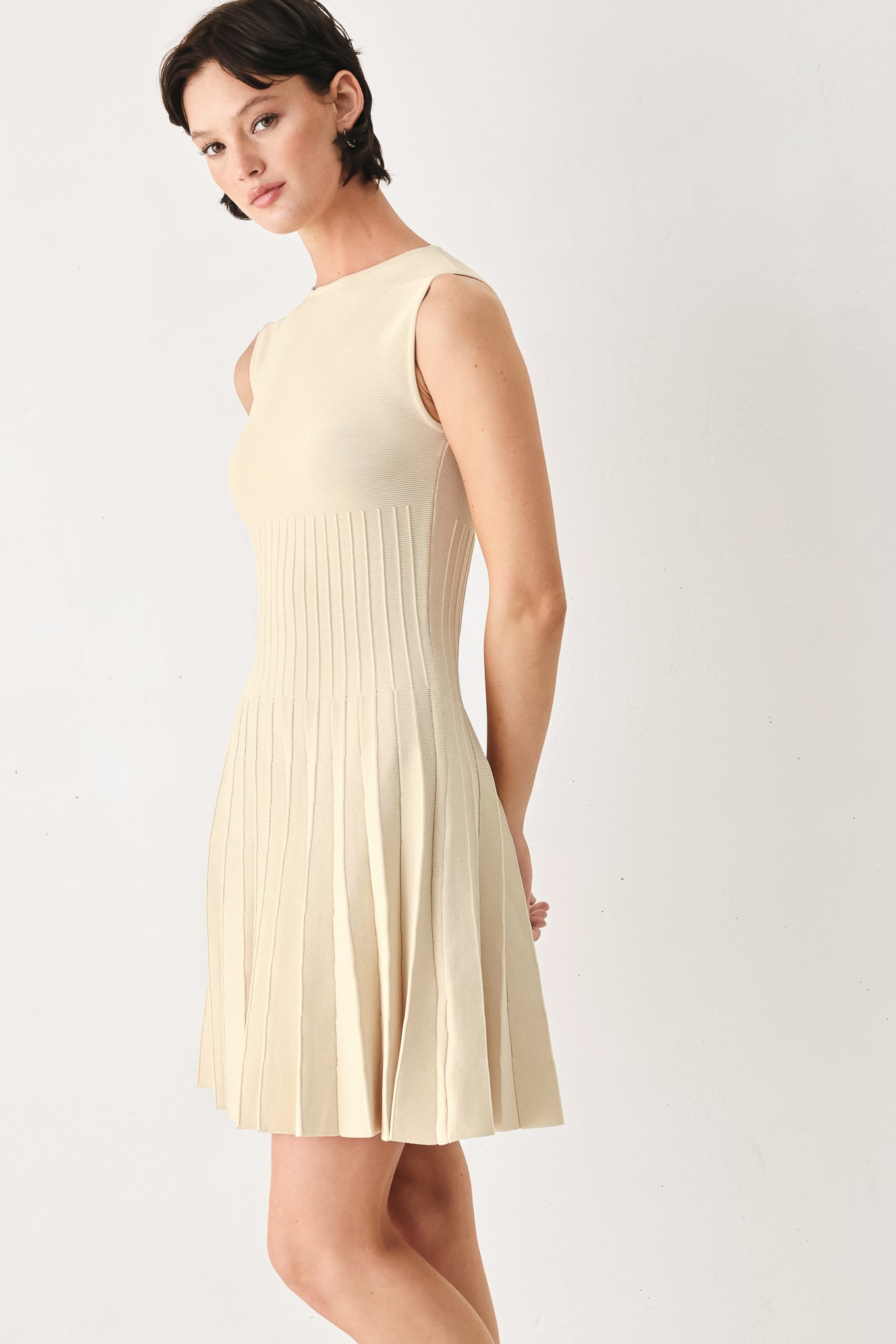 Woman wearing a ivory cream sleeveless sweater knit mini dress with wide neckline, and pleated skirt | FREEMARKET