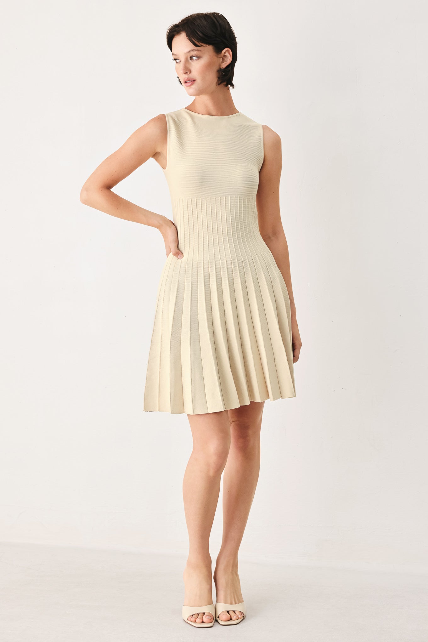 Woman wearing a ivory cream sleeveless sweater knit mini dress with wide neckline, and pleated skirt | FREEMARKET