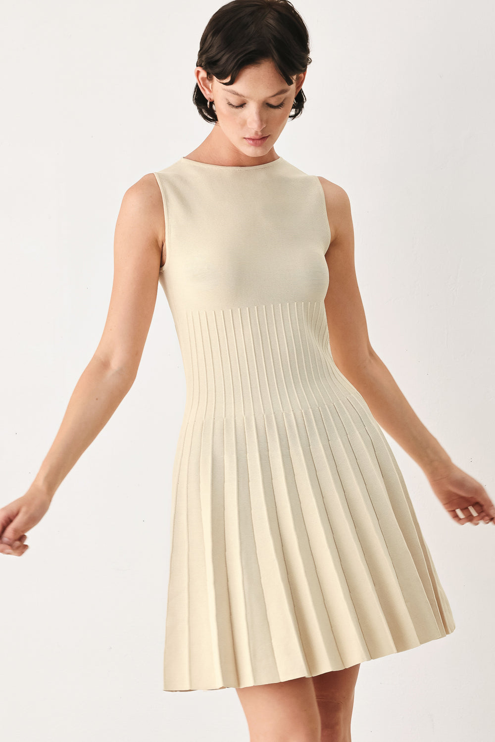 Woman wearing a ivory cream sleeveless sweater knit mini dress with wide neckline, and pleated skirt | FREEMARKET