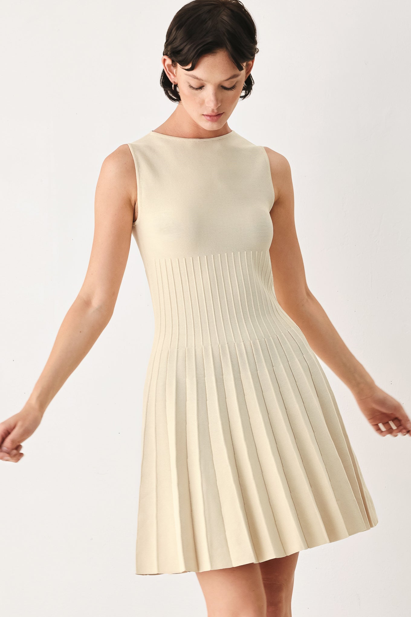 Woman wearing a ivory cream sleeveless sweater knit mini dress with wide neckline, and pleated skirt | FREEMARKET