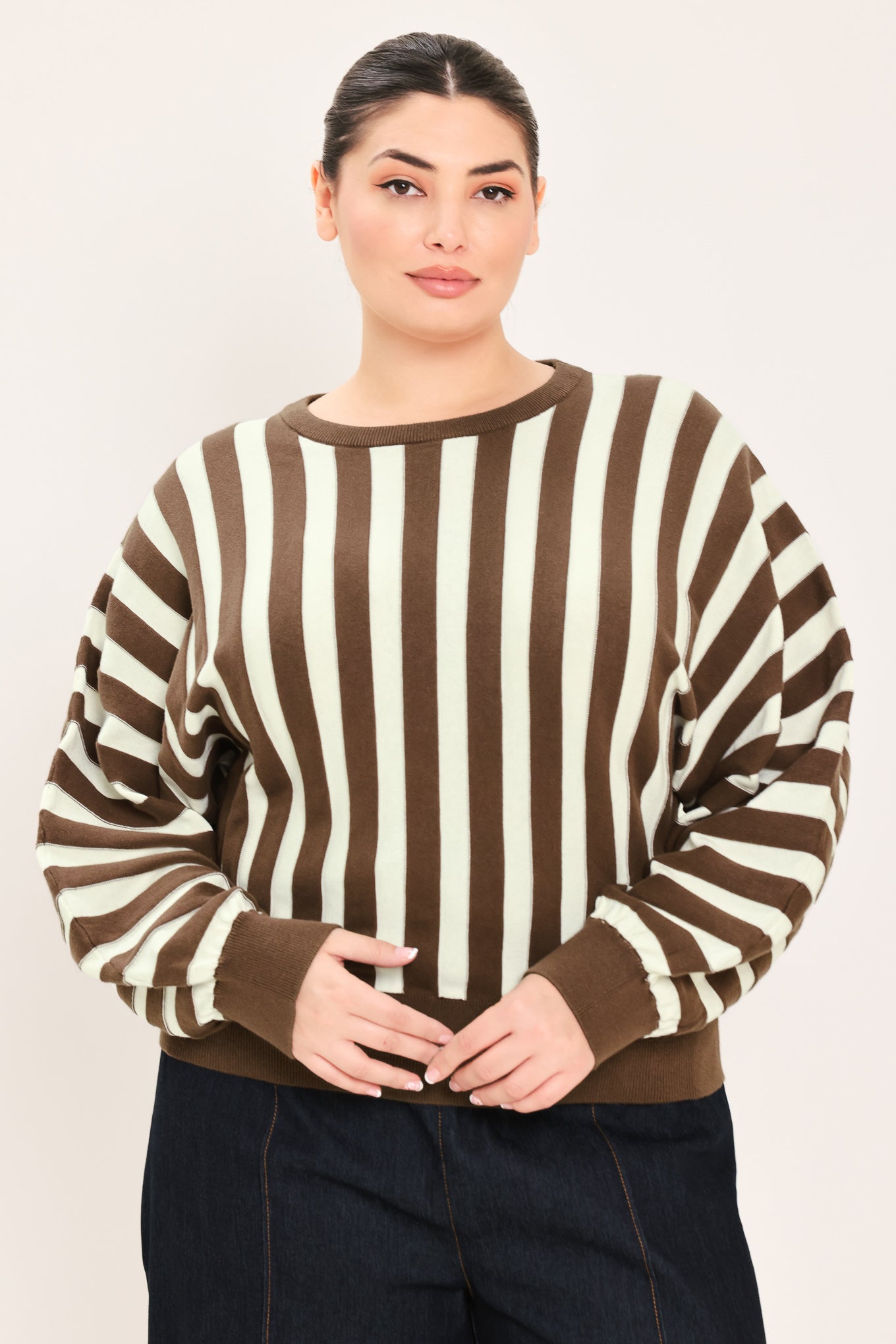 A woman wearing a brown and cream vertical striped knit sweater with long balloon sleeves and ribbed cuffs, paired with dark jeans | Plus Curve Flying Tomato