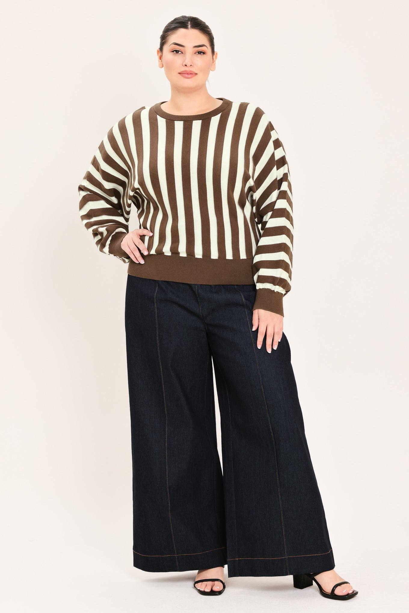A woman wearing a brown and cream vertical striped knit sweater with long balloon sleeves and ribbed cuffs, paired with dark jeans | Plus Curve Flying Tomato