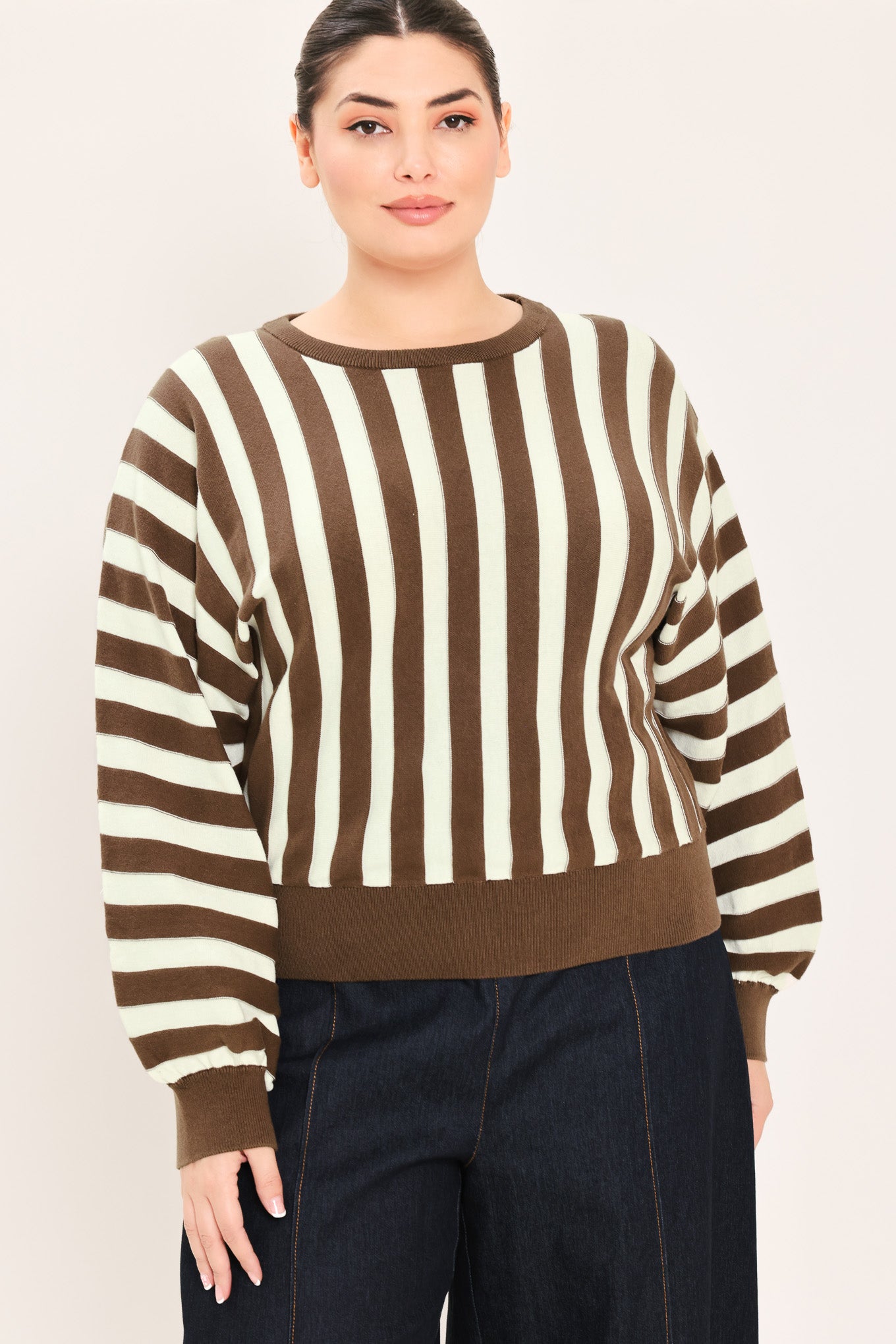 A woman wearing a brown and cream vertical striped knit sweater with long balloon sleeves and ribbed cuffs, paired with dark jeans | Plus Curve Flying Tomato