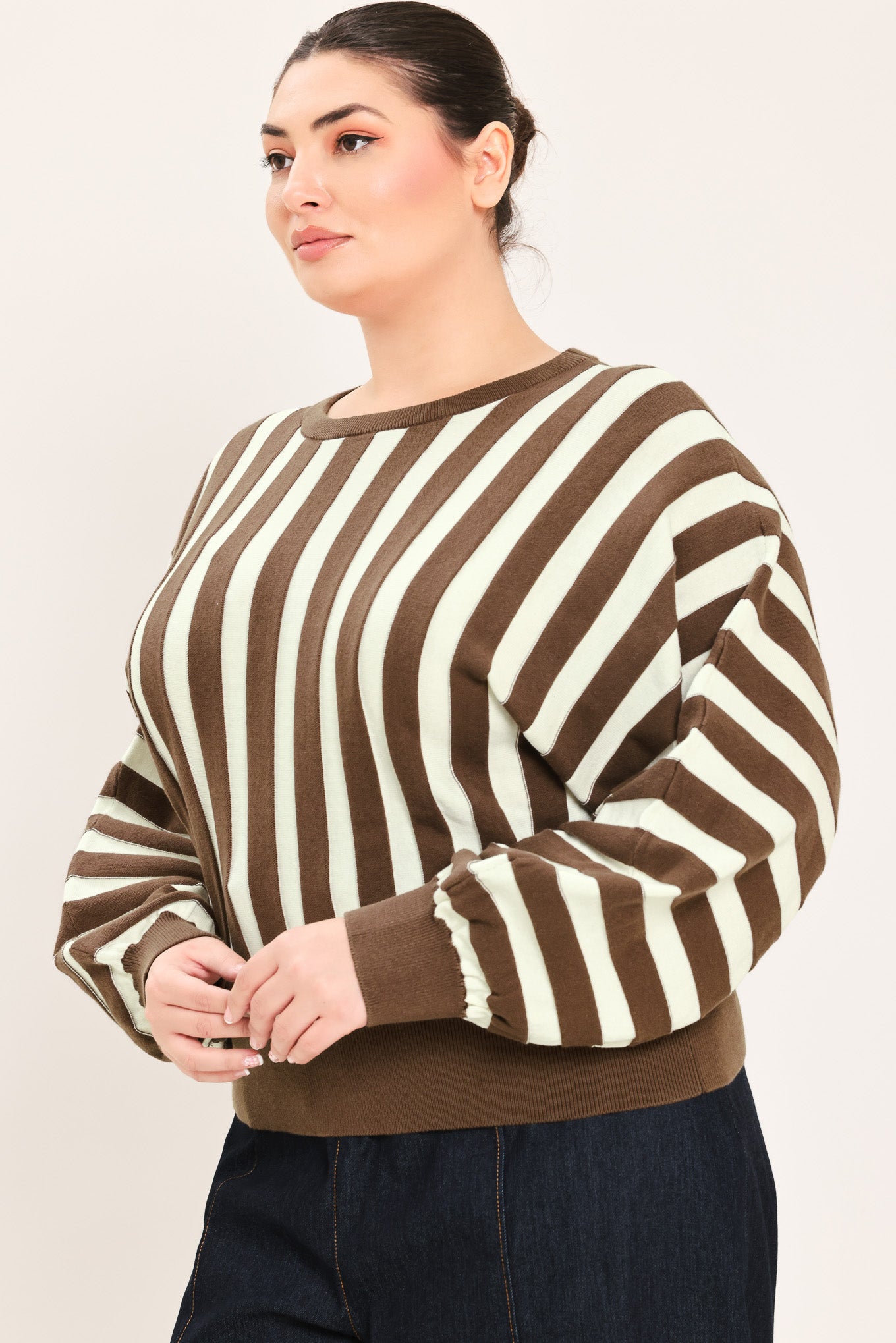A woman wearing a brown and cream vertical striped knit sweater with long balloon sleeves and ribbed cuffs, paired with dark jeans | Plus Curve Flying Tomato