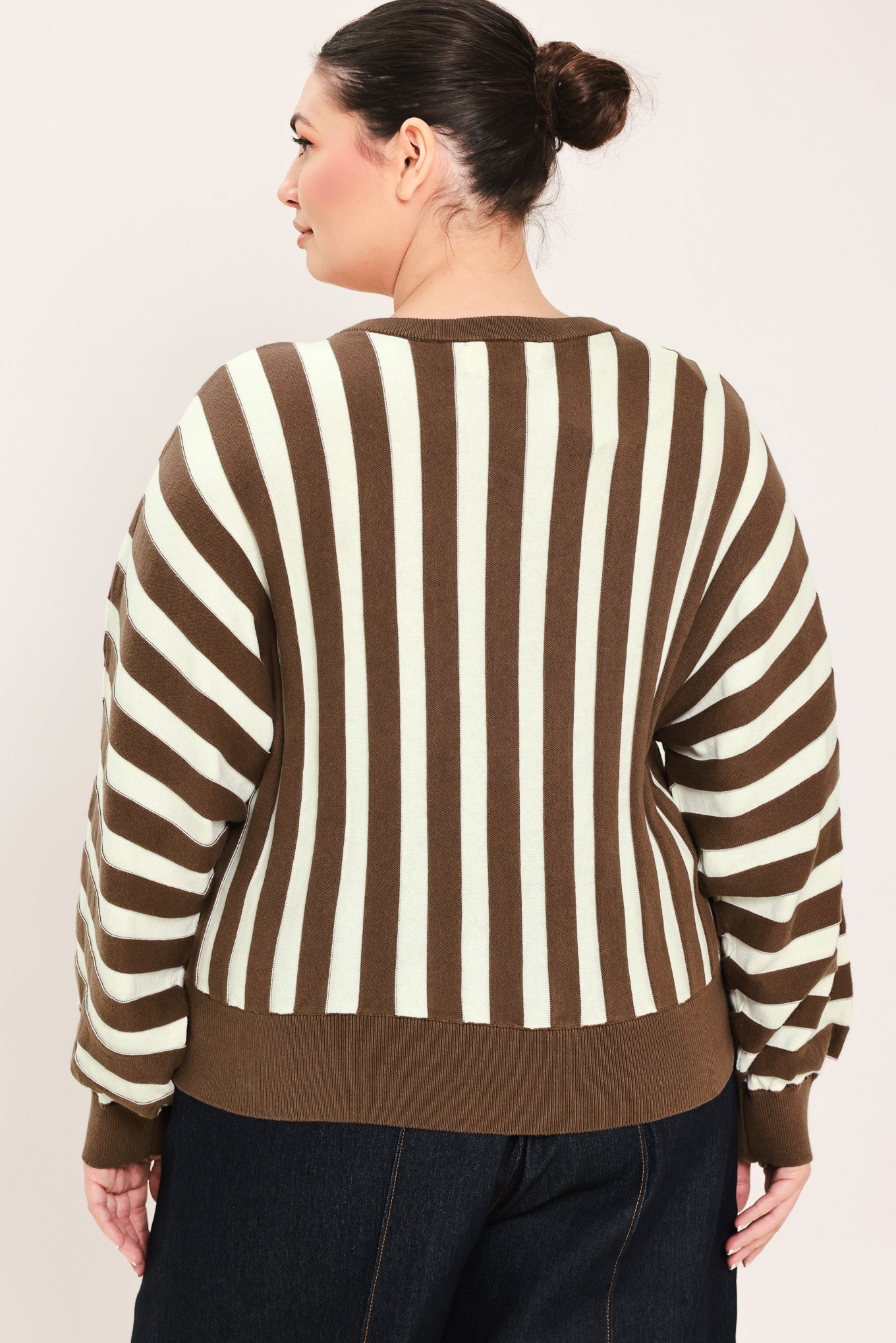 A woman wearing a brown and cream vertical striped knit sweater with long balloon sleeves and ribbed cuffs, paired with dark jeans | Plus Curve Flying Tomato