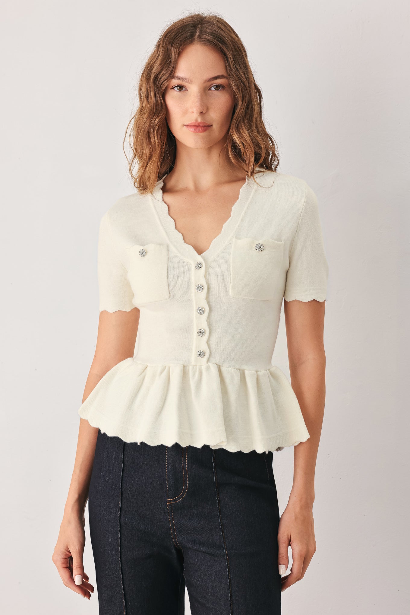 A woman wearing a short-sleeve off-white sweater knit blouse with a scalloped V-neckline, front buttons, and chest pockets | FREEMARKET
