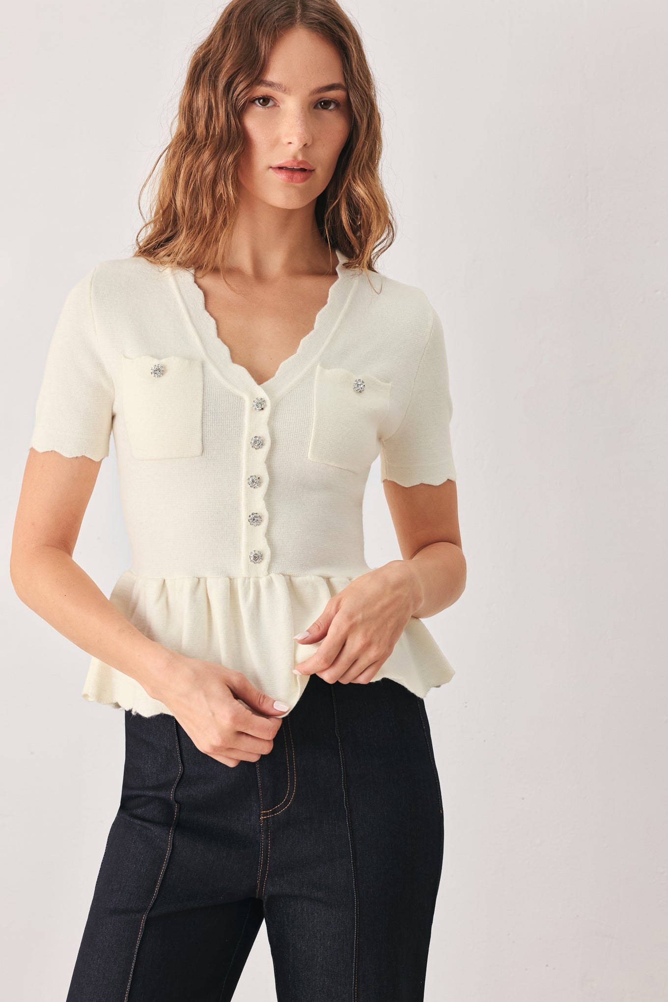 A woman wearing a short-sleeve off-white sweater knit blouse with a scalloped V-neckline, front buttons, and chest pockets | FREEMARKET