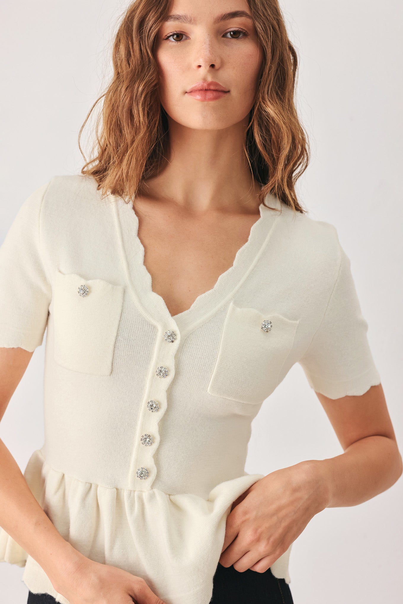 A woman wearing a short-sleeve off-white sweater knit blouse with a scalloped V-neckline, front buttons, and chest pockets | FREEMARKET