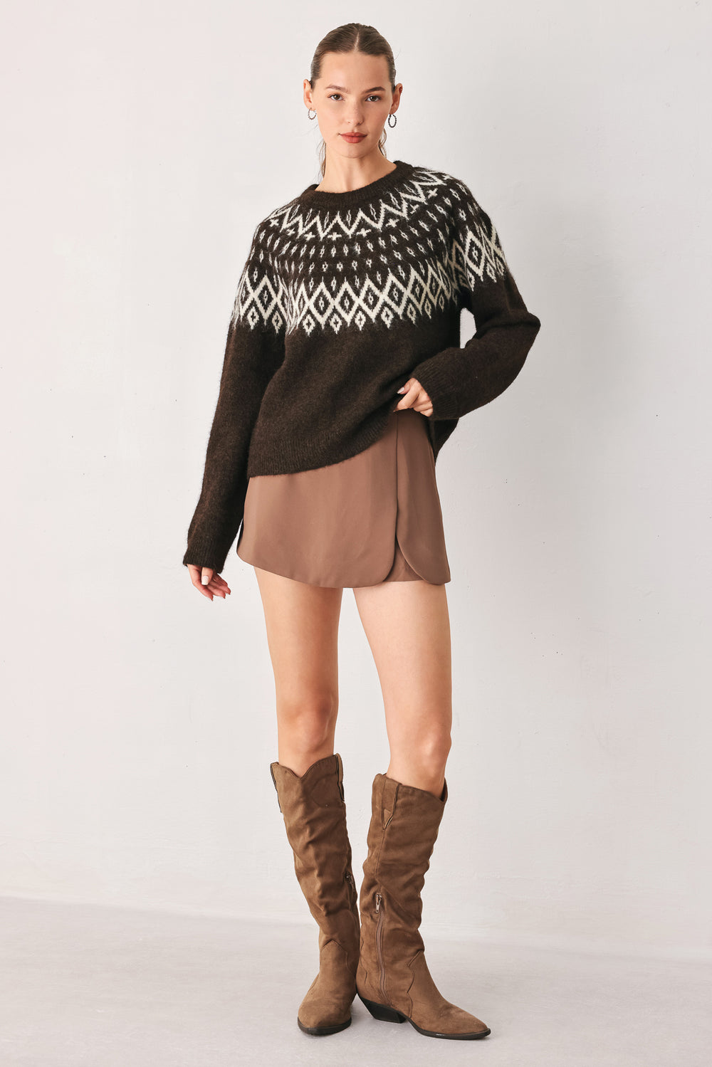 A model stands against a light gray studio background wearing a dark brown knit sweater with a white geometric pattern across the chest | FREEMARKET