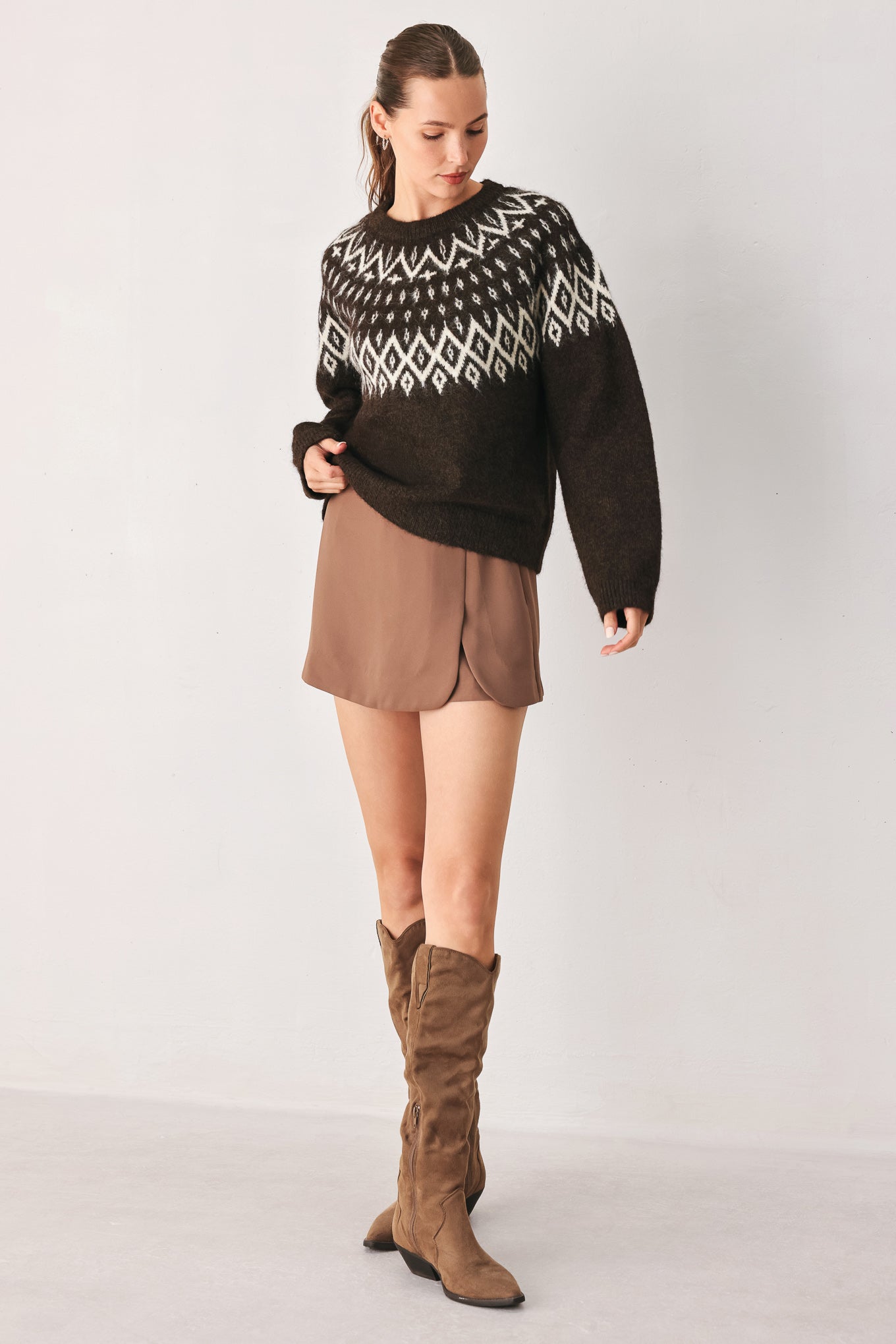 A model stands against a light gray studio background wearing a dark brown knit sweater with a white geometric pattern across the chest | FREEMARKET