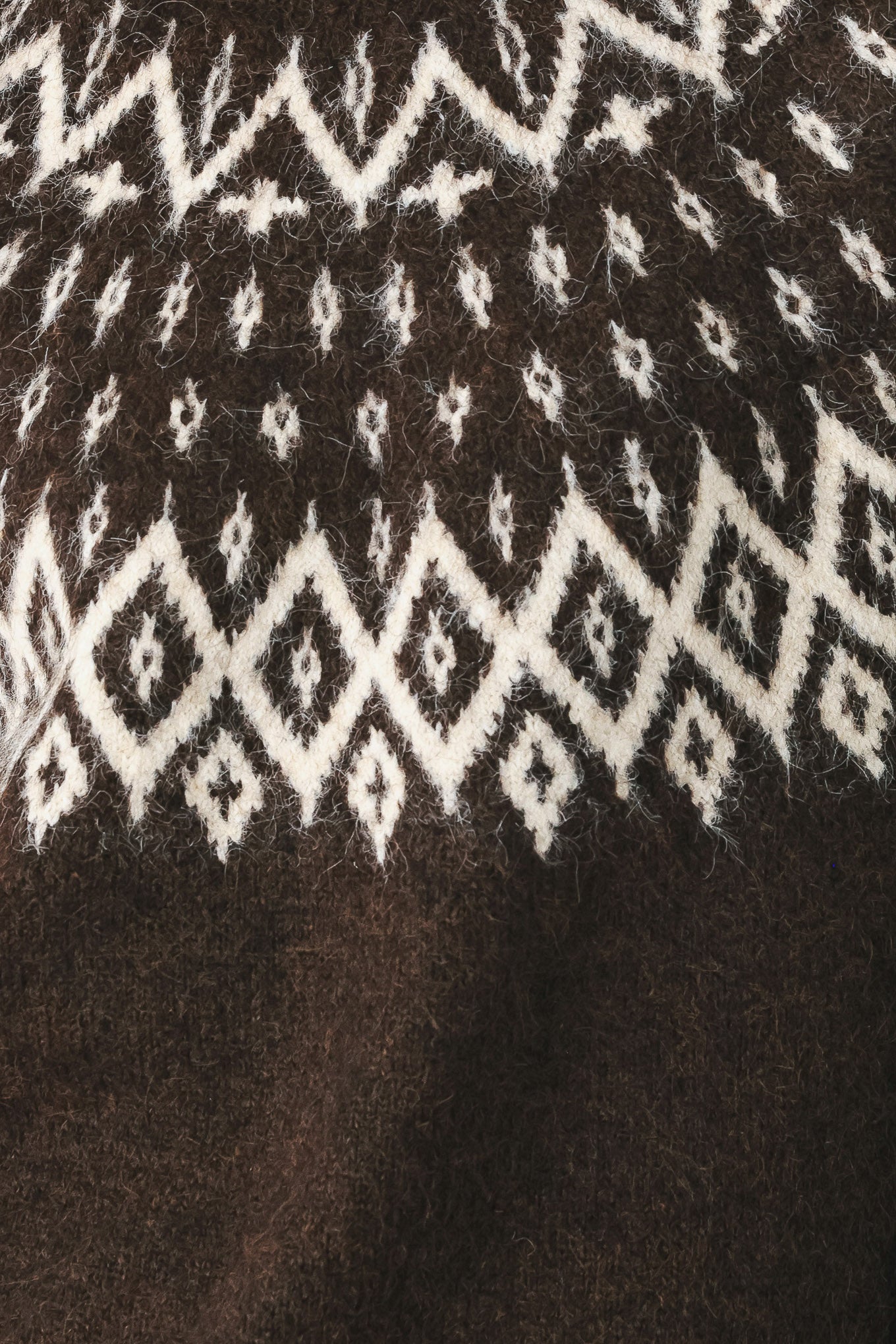 A model stands against a light gray studio background wearing a dark brown knit sweater with a white geometric pattern across the chest | FREEMARKET