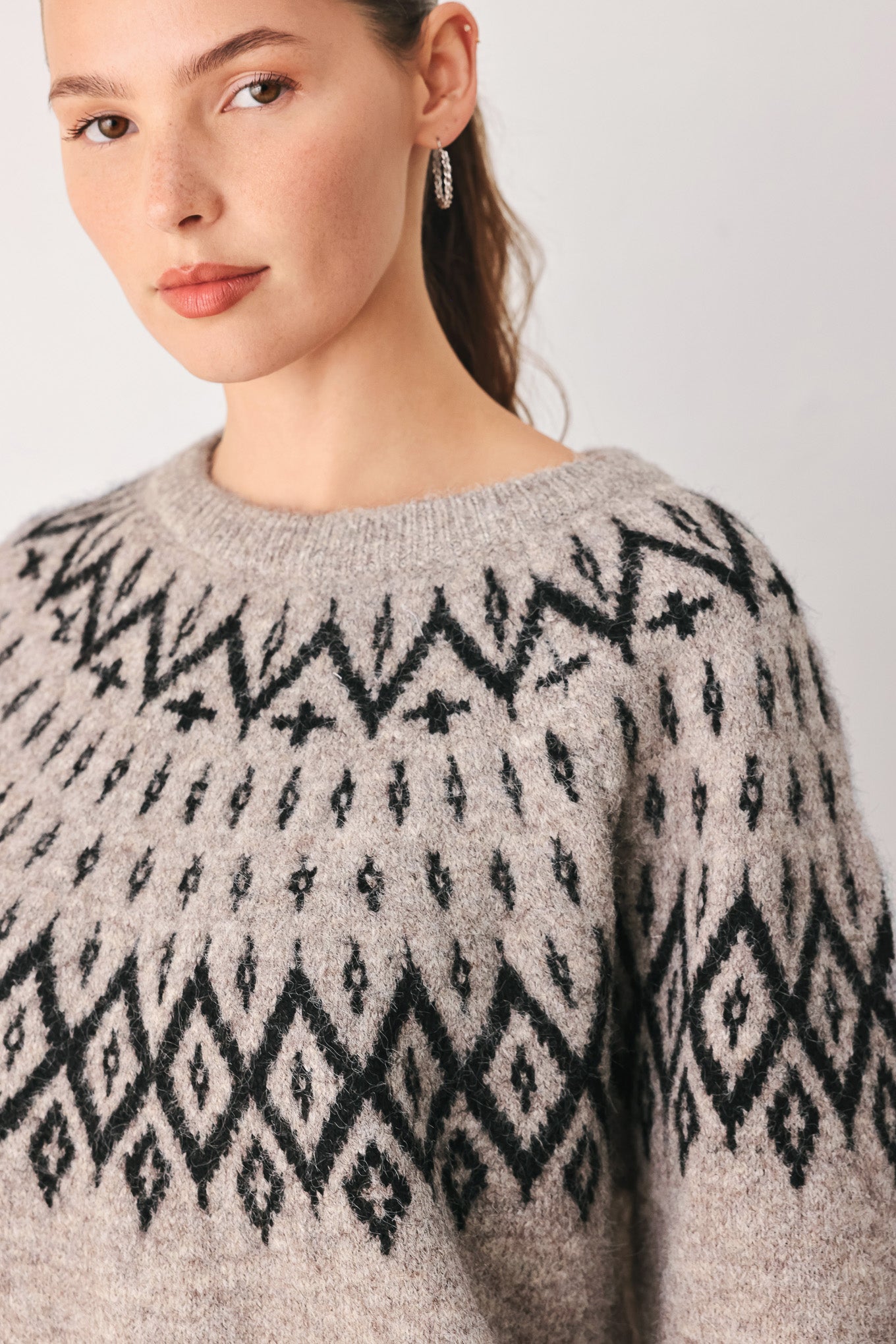 A model wearing a taupe knit sweater with a black geometric pattern across the chest | FREEMARKET