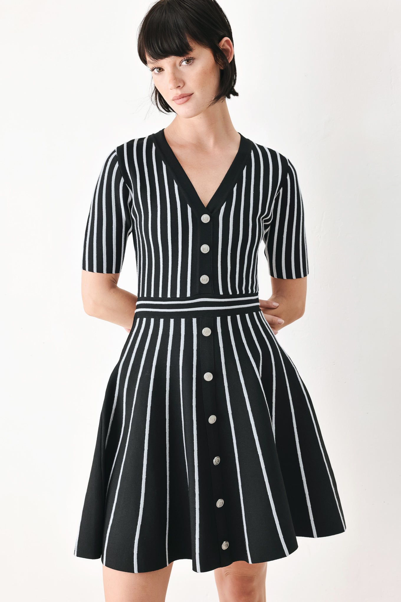 A woman modeling a short-sleeve V-neck dress with vertical black and silver stripes, a buttoned front, and a flared skirt | FREEMARKET