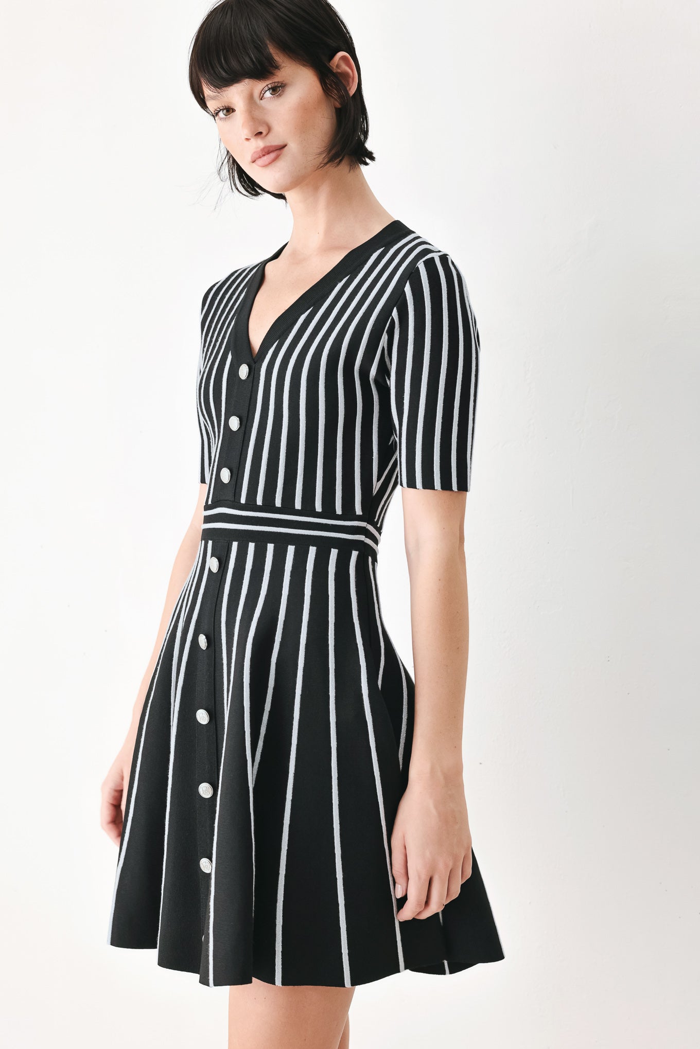 A woman modeling a short-sleeve V-neck dress with vertical black and silver stripes, a buttoned front, and a flared skirt | FREEMARKET
