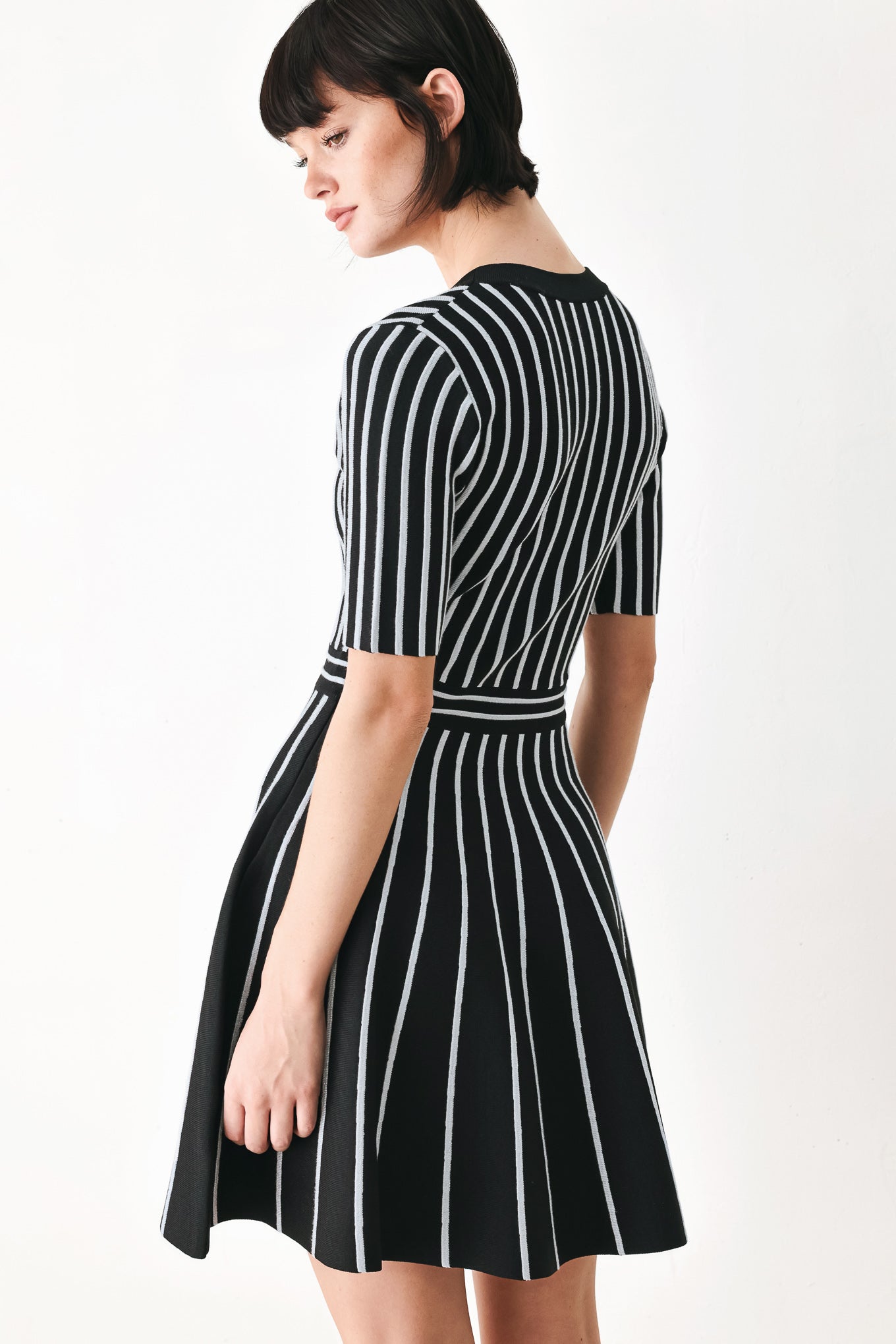 A woman modeling a short-sleeve V-neck dress with vertical black and silver stripes, a buttoned front, and a flared skirt | FREEMARKET