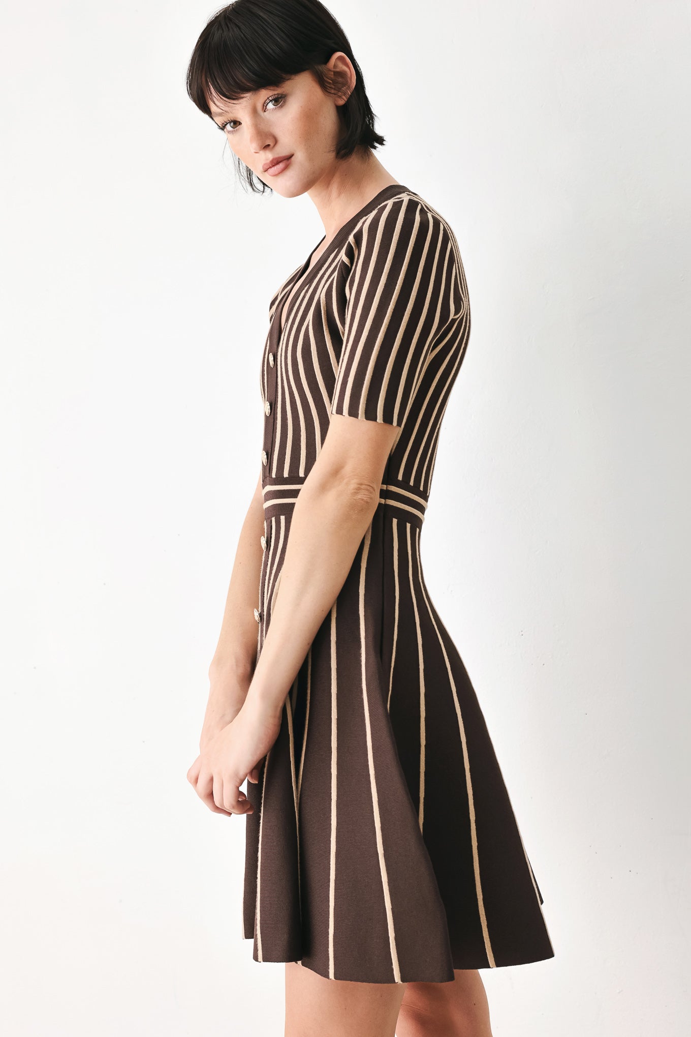 A woman modeling a short-sleeve V-neck dress with vertical brown and beige stripes, a buttoned front, and a flared skirt | FREEMARKET