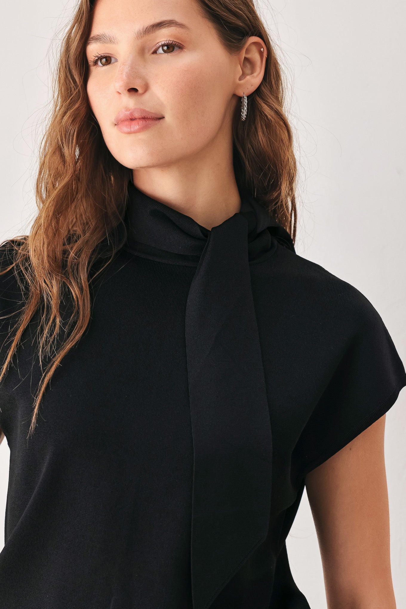 A woman wearing a black short-sleeve knit top with a high mock neck and a large draped tie detail at the front | FREEMARKET