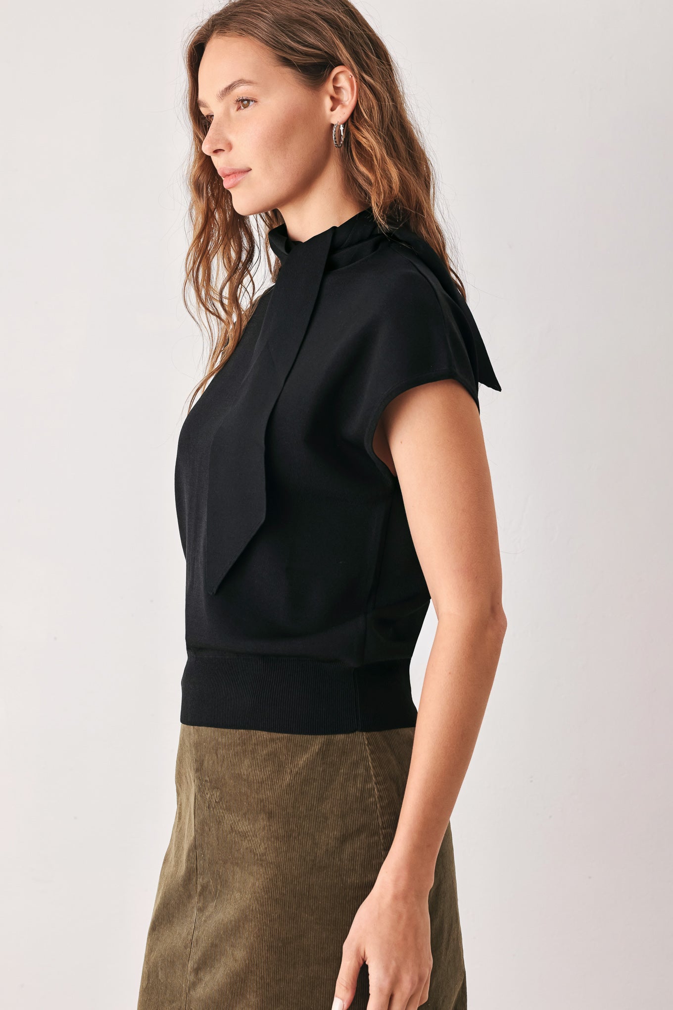A woman wearing a black short-sleeve knit top with a high mock neck and a large draped tie detail at the front | FREEMARKET