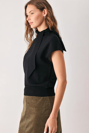 A woman wearing a black short-sleeve knit top with a high mock neck and a large draped tie detail at the front | FREEMARKET