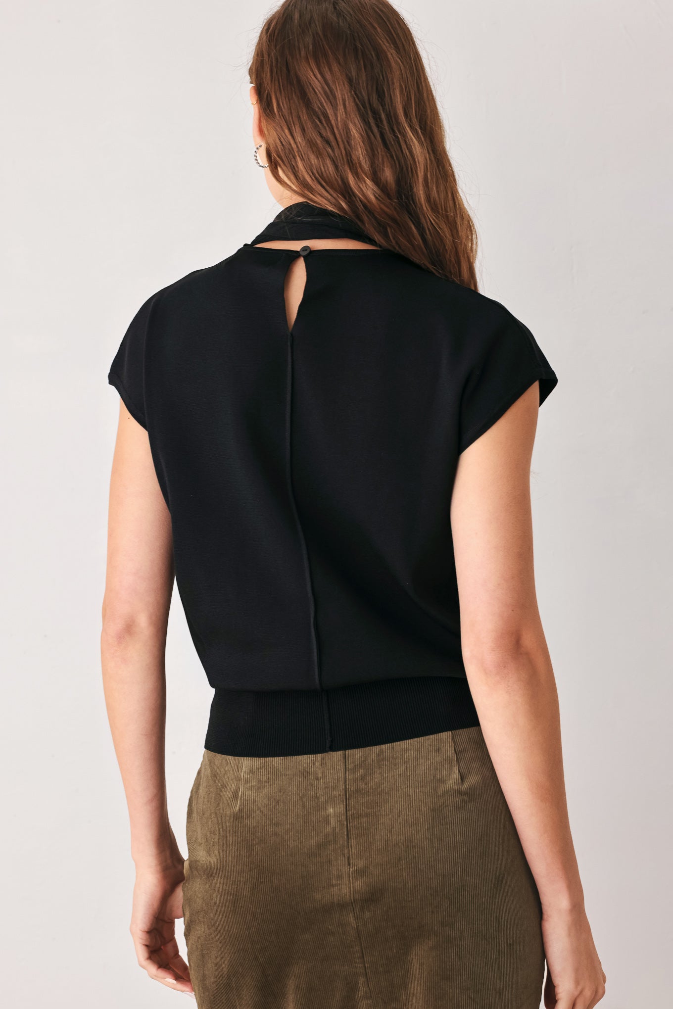 A woman wearing a black short-sleeve knit top with a high mock neck and a large draped tie detail at the front | FREEMARKET