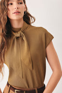 A woman wearing a camel short-sleeve knit top with a high mock neck and a large draped tie detail at the front | FREEMARKET