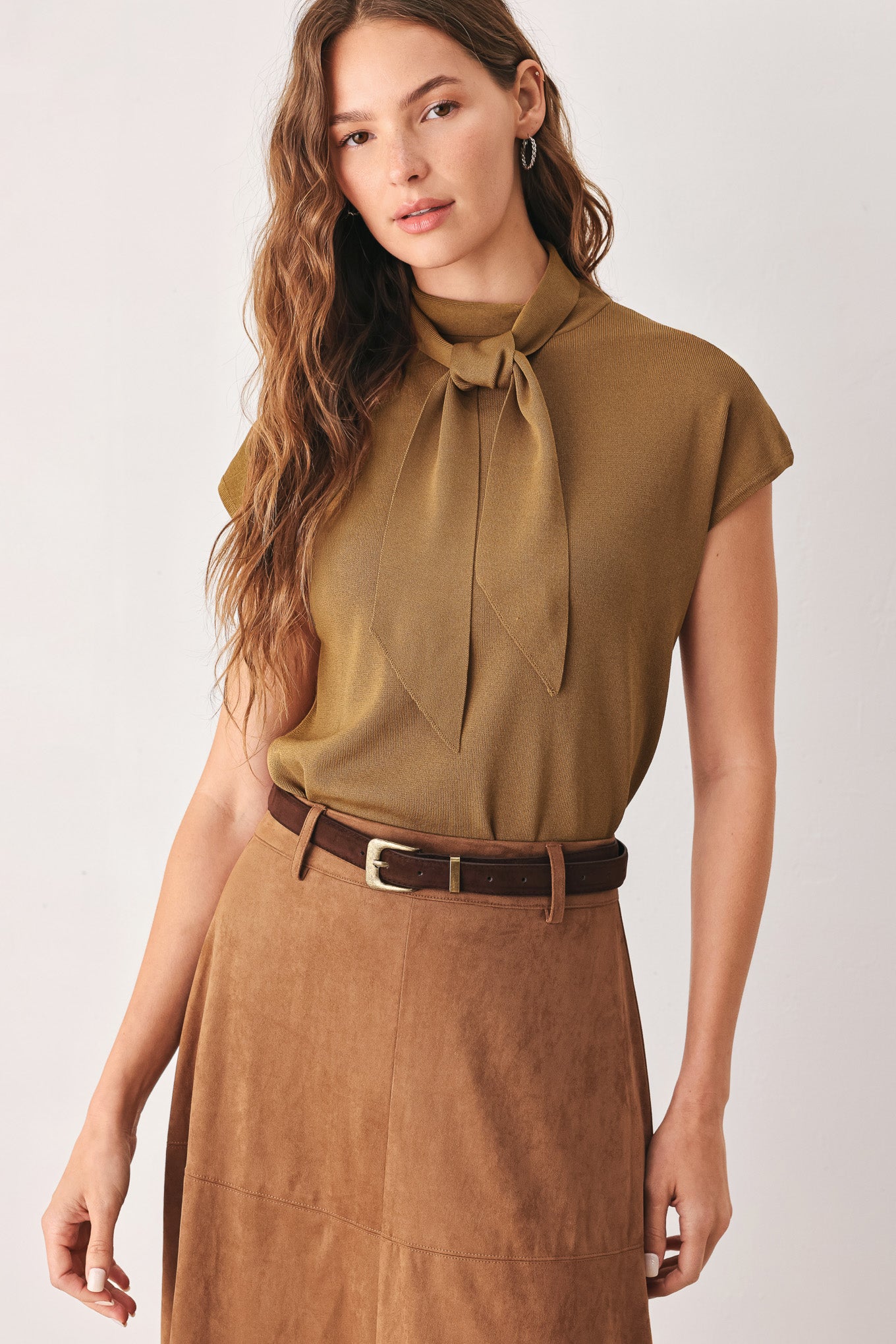 A woman wearing a camel short-sleeve knit top with a high mock neck and a large draped tie detail at the front | FREEMARKET