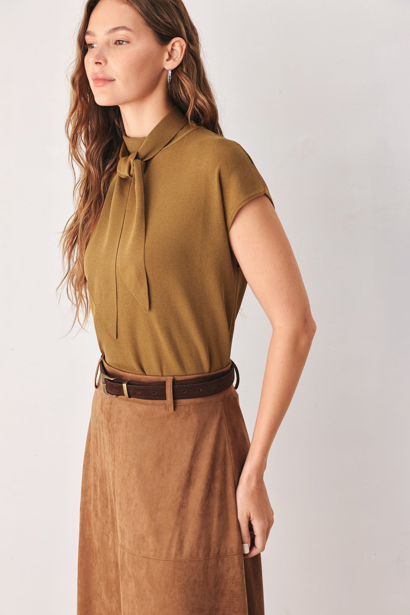 A woman wearing a camel short-sleeve knit top with a high mock neck and a large draped tie detail at the front | FREEMARKET
