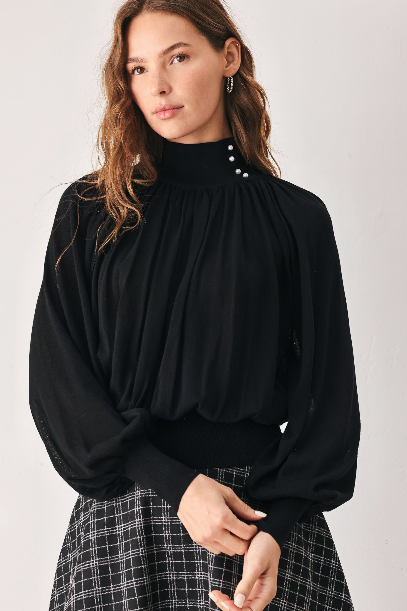 A woman wearing a black long-sleeve blouse with a high gathered neckline and pearl-like embellishments | FREEMARKET