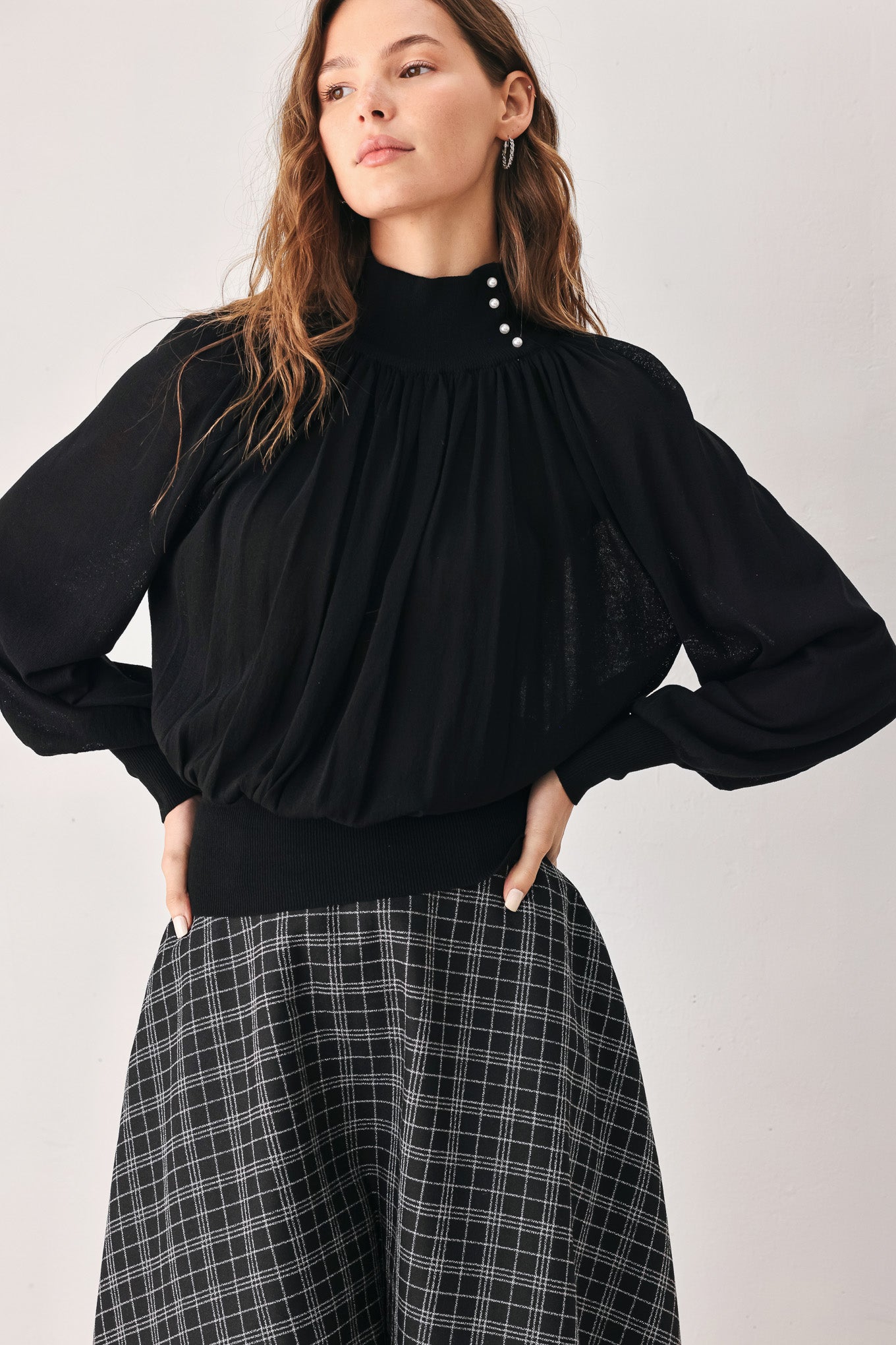 A woman wearing a black long-sleeve blouse with a high gathered neckline and pearl-like embellishments | FREEMARKET