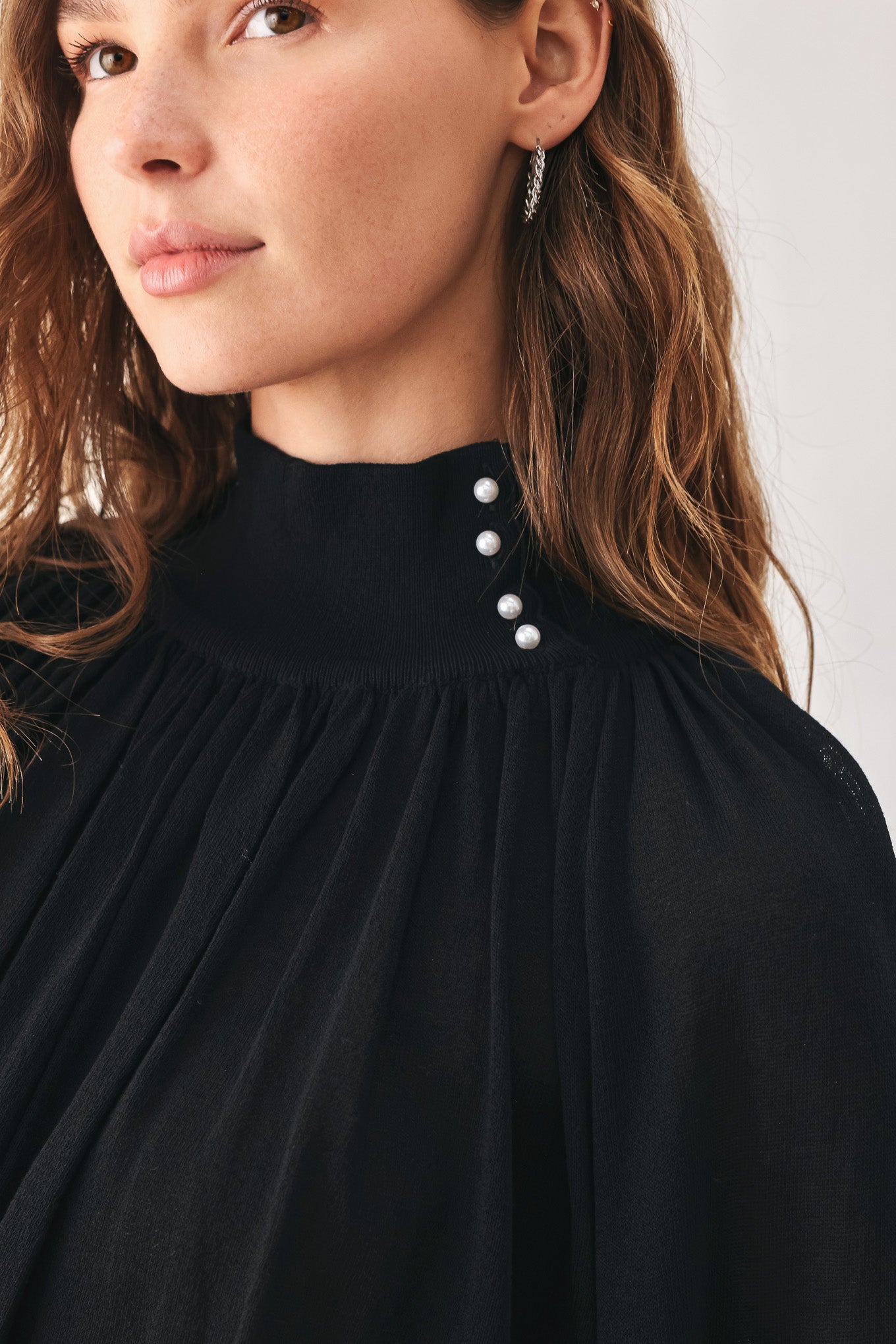 A woman wearing a black long-sleeve blouse with a high gathered neckline and pearl-like embellishments | FREEMARKET