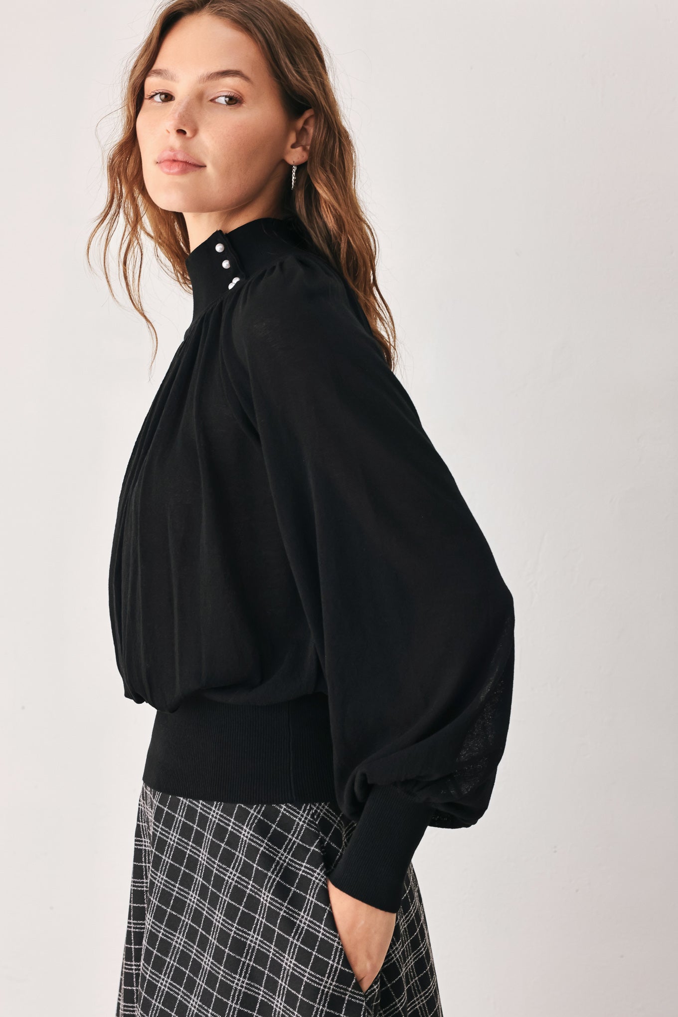 A woman wearing a black long-sleeve blouse with a high gathered neckline and pearl-like embellishments | FREEMARKET