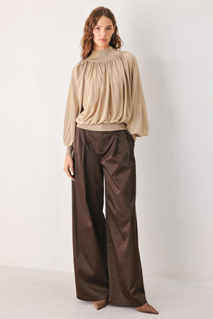 A woman wearing a taupe long-sleeve blouse with a high gathered neckline and pearl-like embellishments | FREEMARKET