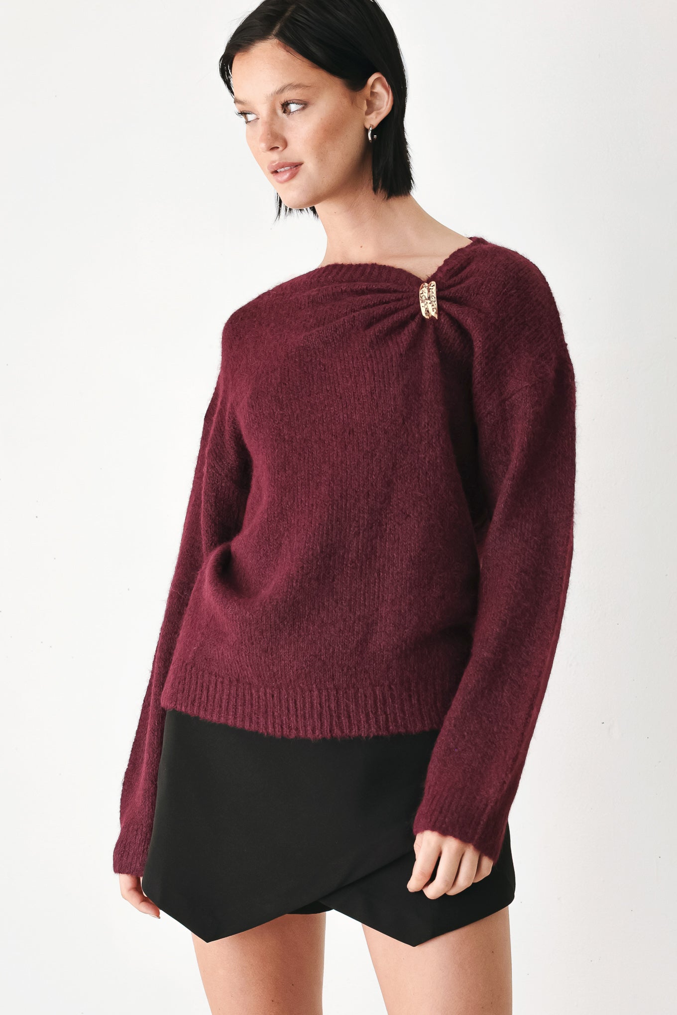 A woman modeling a dark burgundy knit sweater with a unique draped neckline and a small gold button accent | FREEMARKET