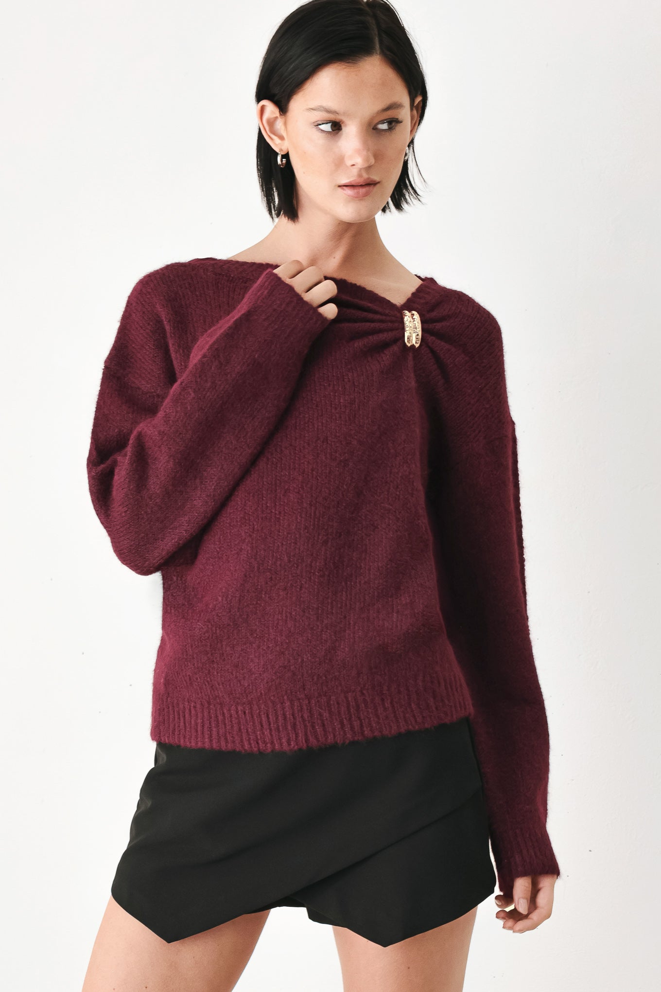 A woman modeling a dark burgundy knit sweater with a unique draped neckline and a small gold button accent | FREEMARKET