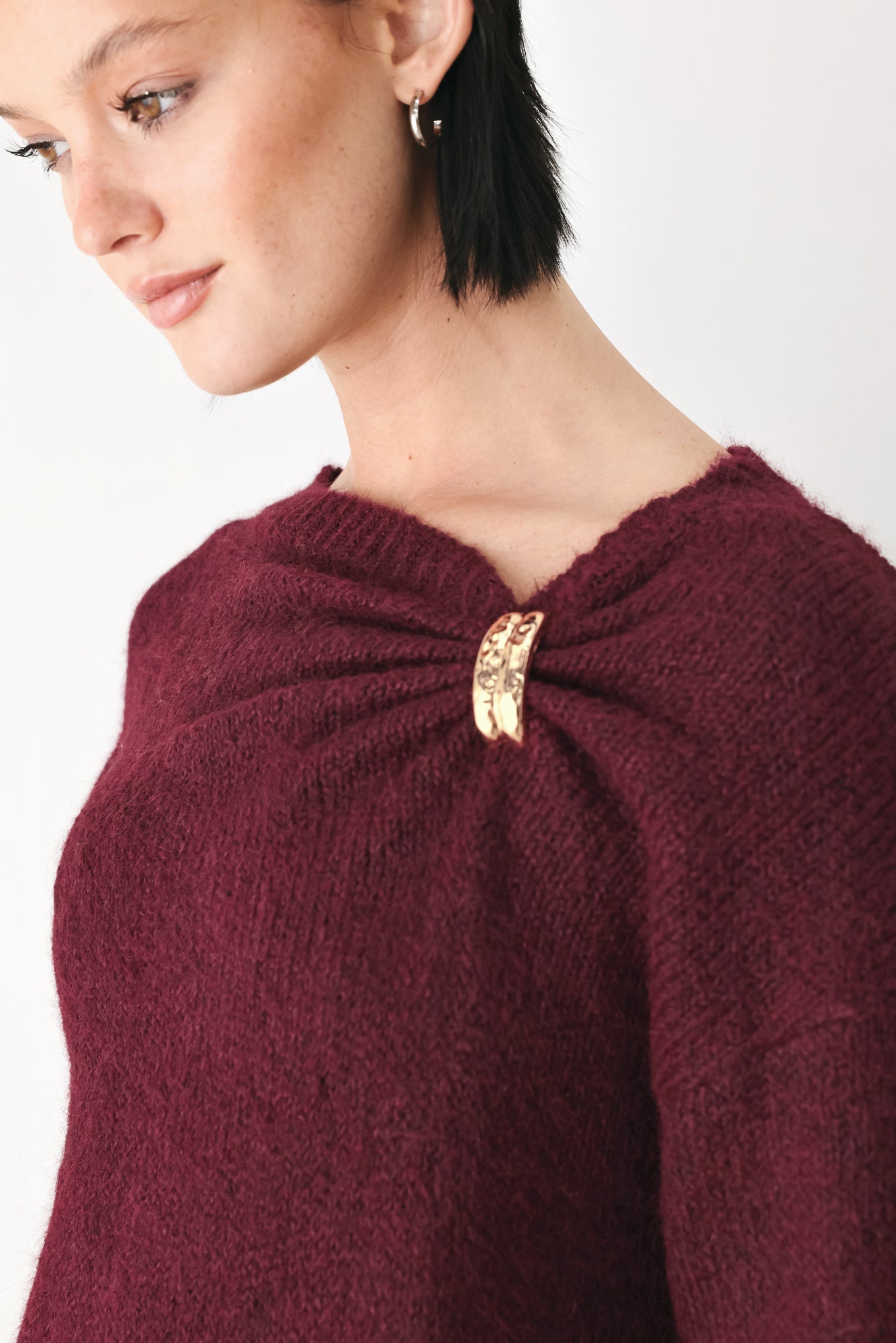 A woman modeling a dark burgundy knit sweater with a unique draped neckline and a small gold button accent | FREEMARKET