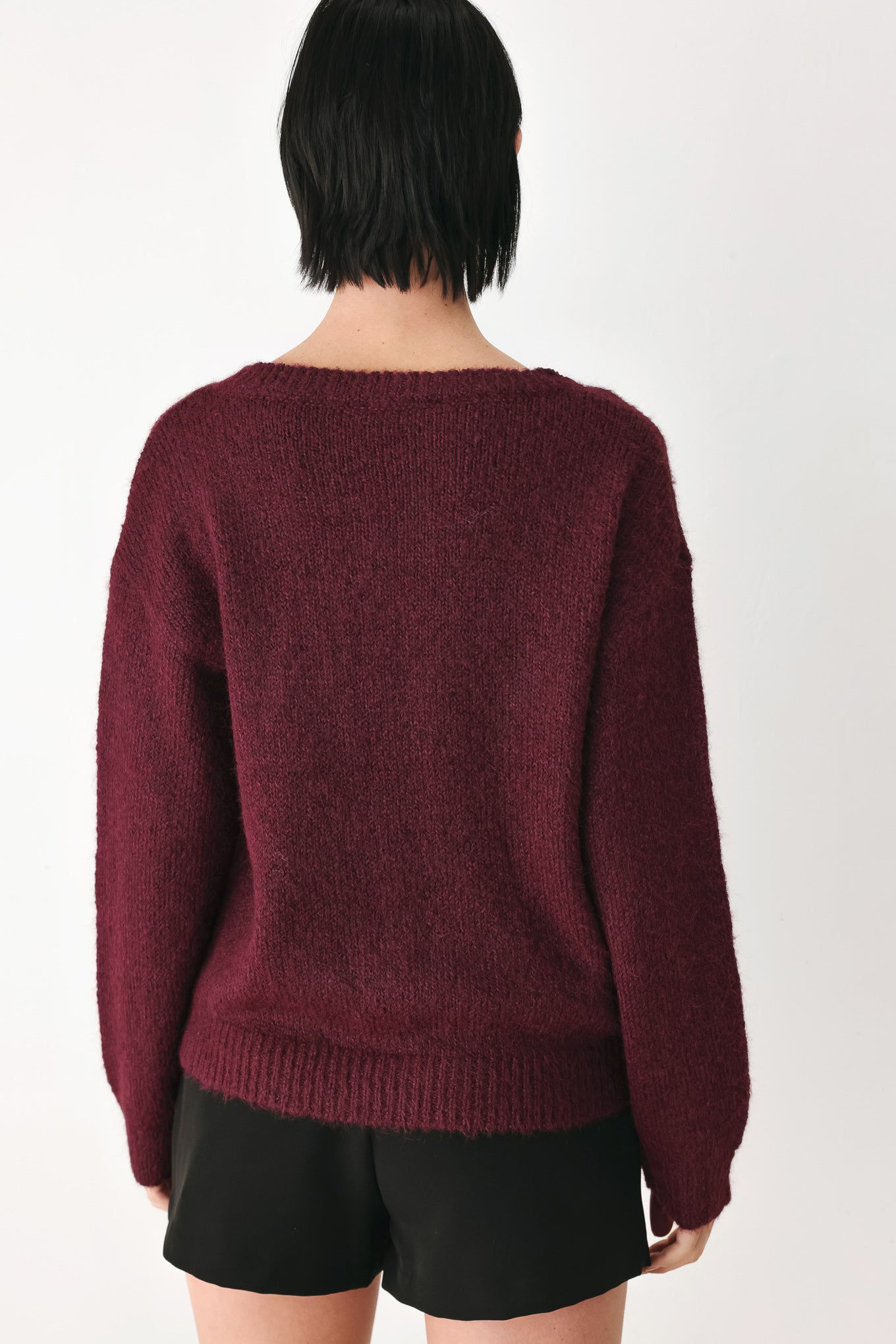 A woman modeling a dark burgundy knit sweater with a unique draped neckline and a small gold button accent | FREEMARKET